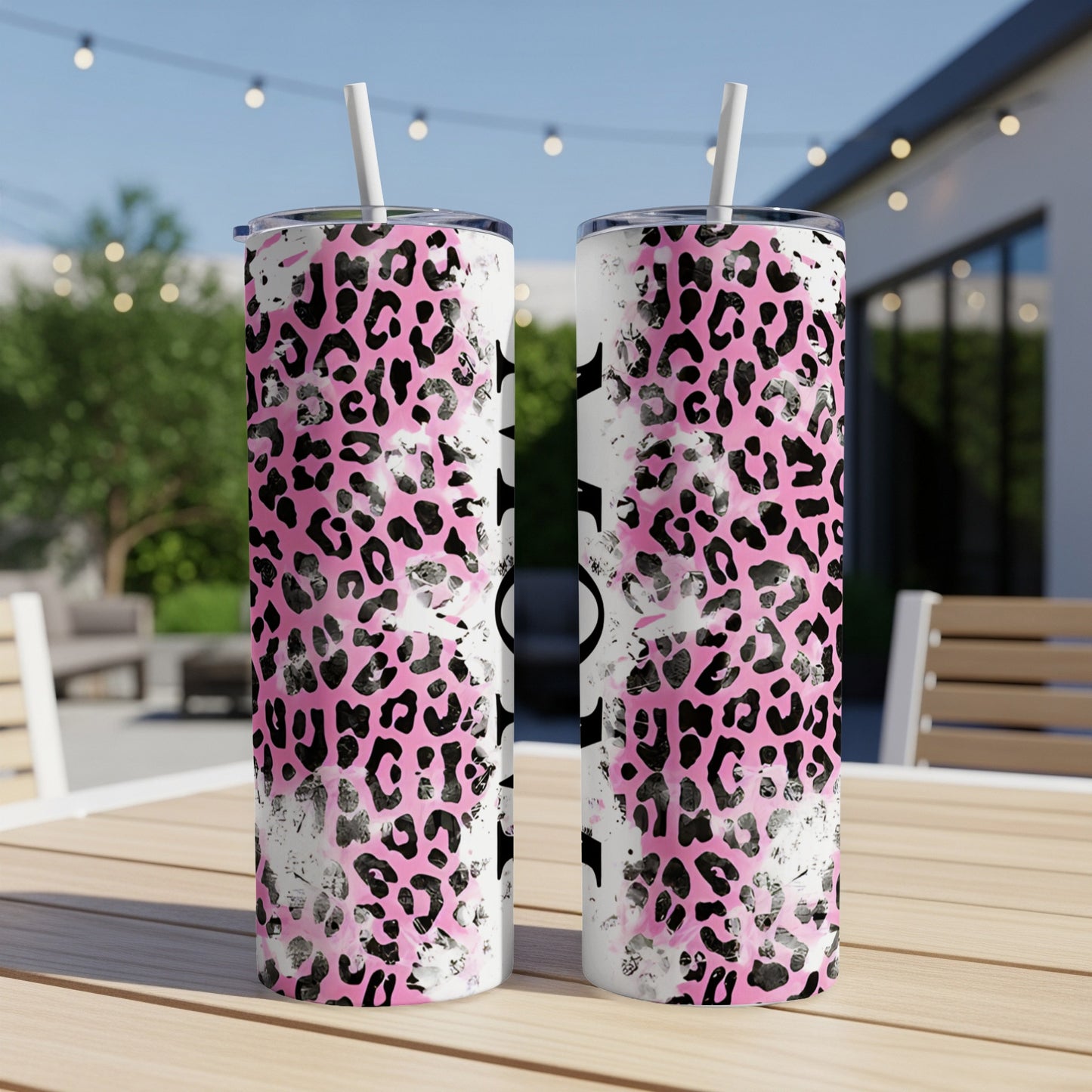 Two pink leopard print tumblers with straws on a table.
