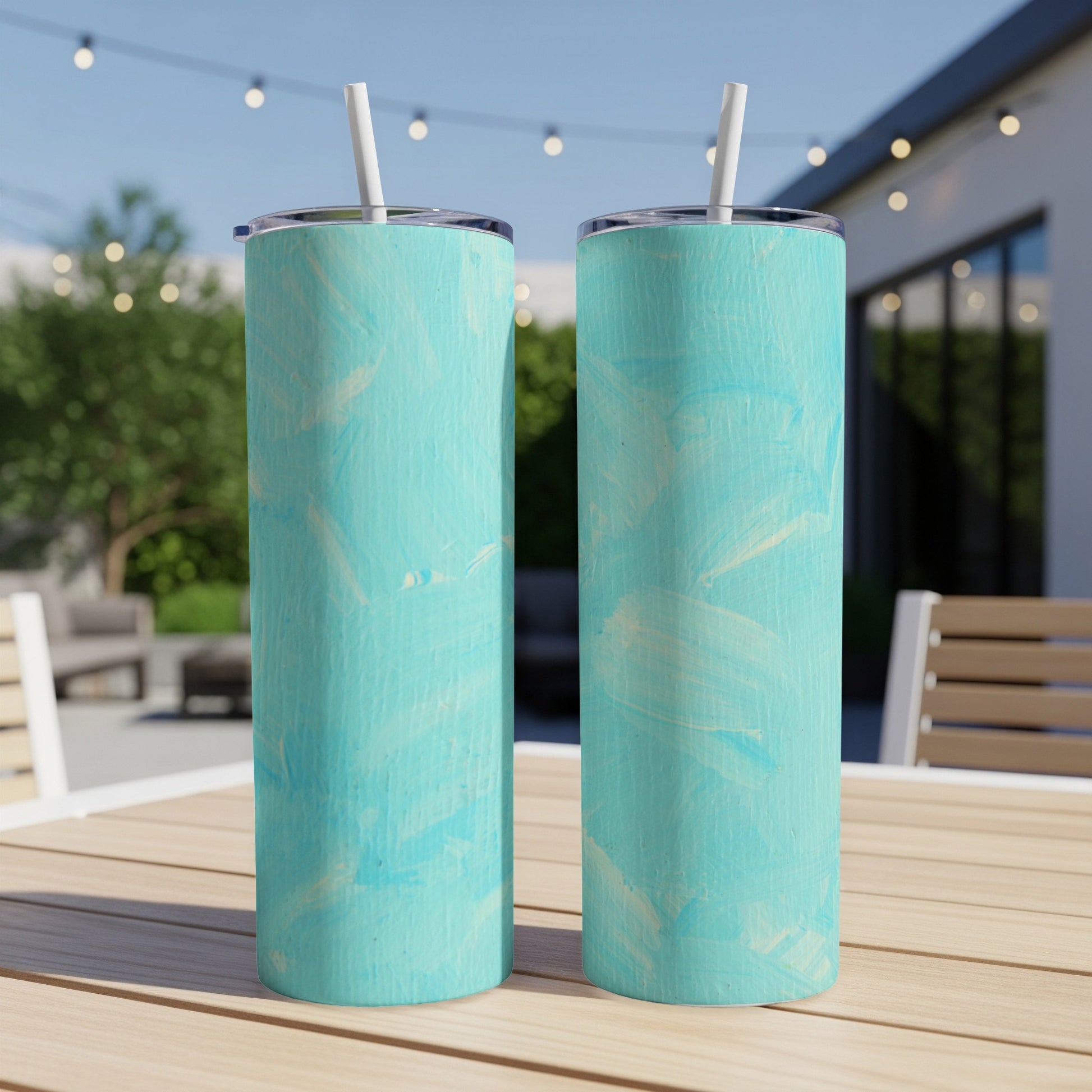 Two aqua teal abstract textured tumblers with straws on a table.