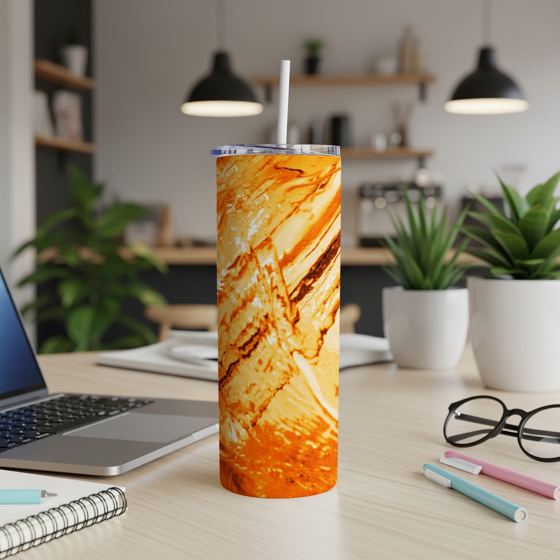 Orange marble tumbler with straw on a desk next to a laptop.