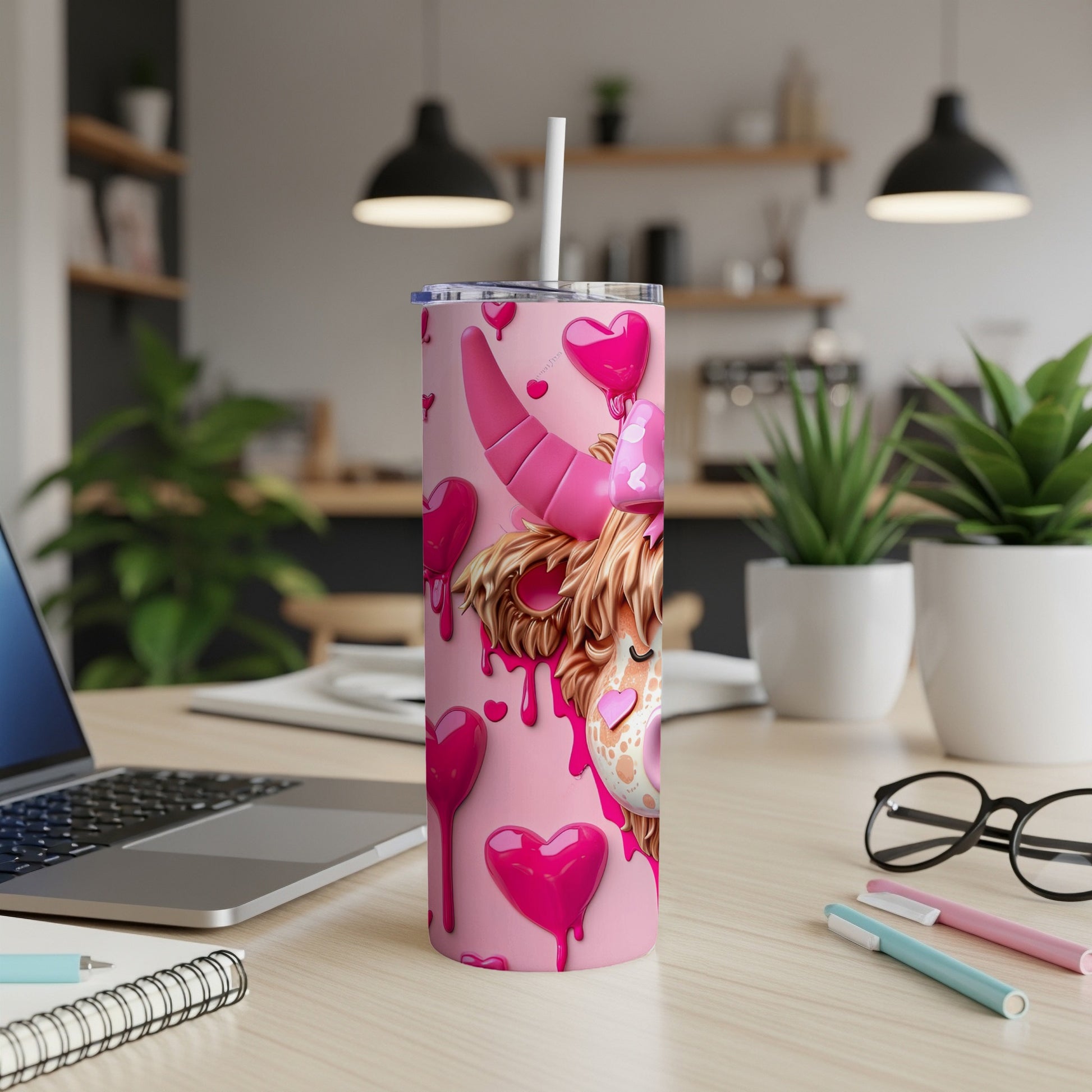 Pink cow tumbler with hearts and a straw on a desk.