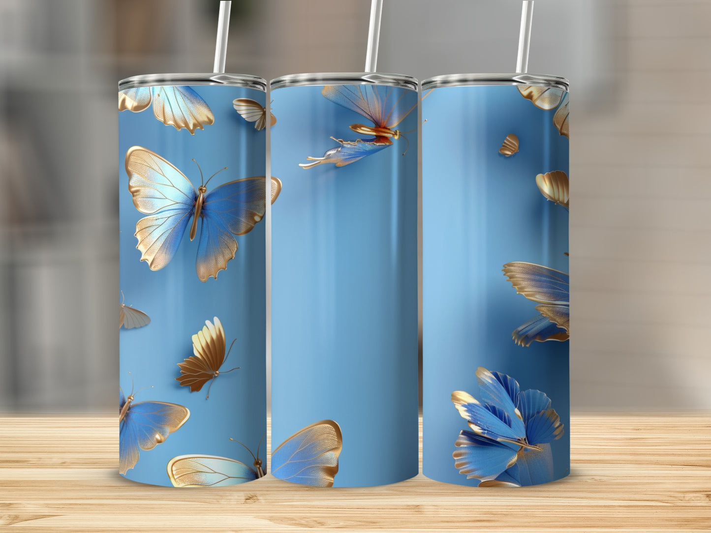 Three blue tumblers with gold butterfly designs on a wooden surface.