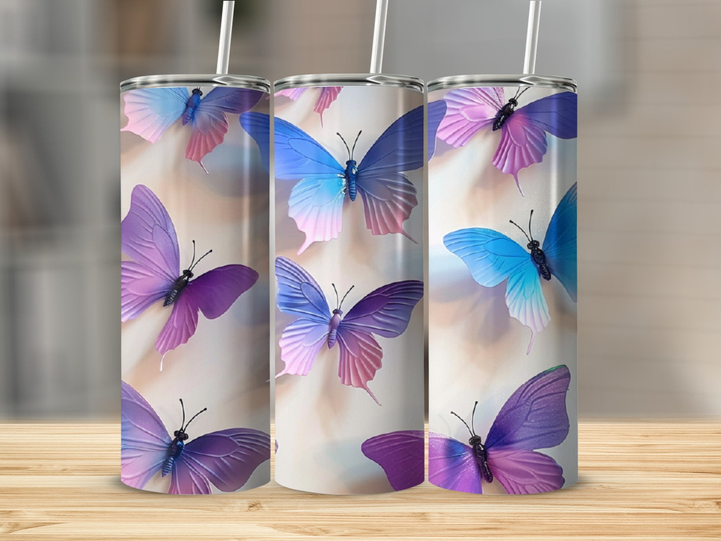 Three tumblers with colorful butterfly designs on a wooden surface.