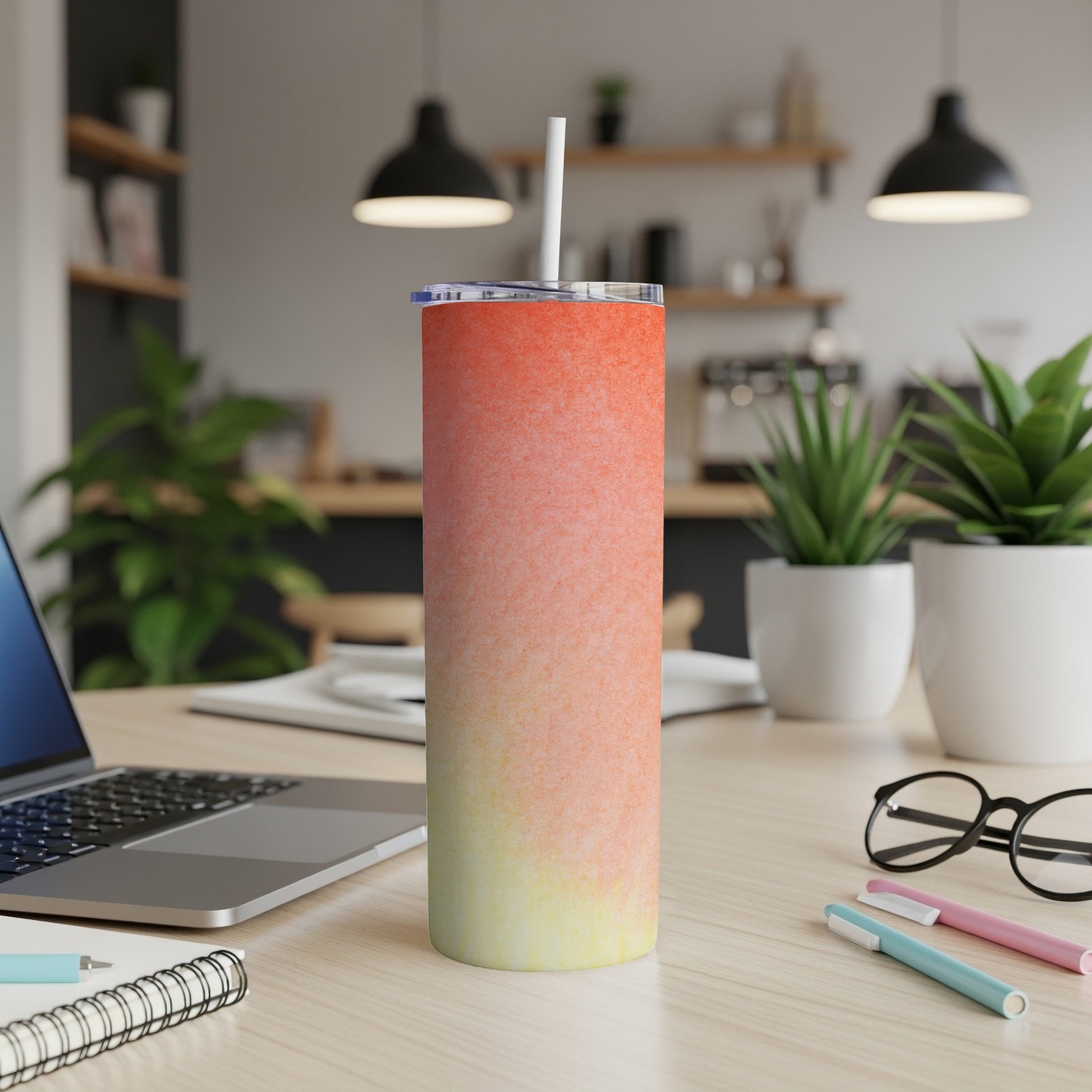 Tumbler with gradient orange and yellow design on a desk with laptop and pens.