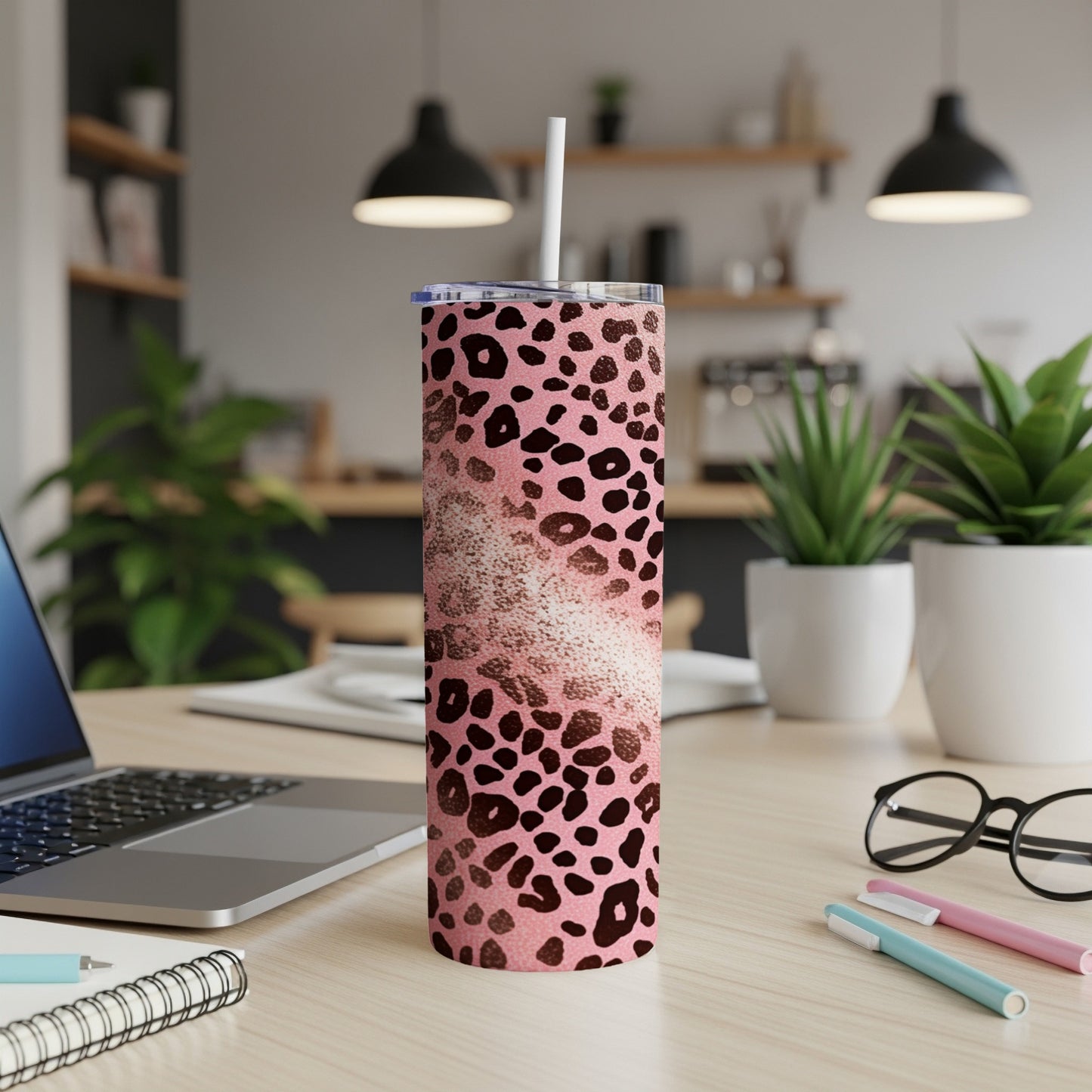Pink leopard print tumbler with straw on a desk with a laptop and pens.