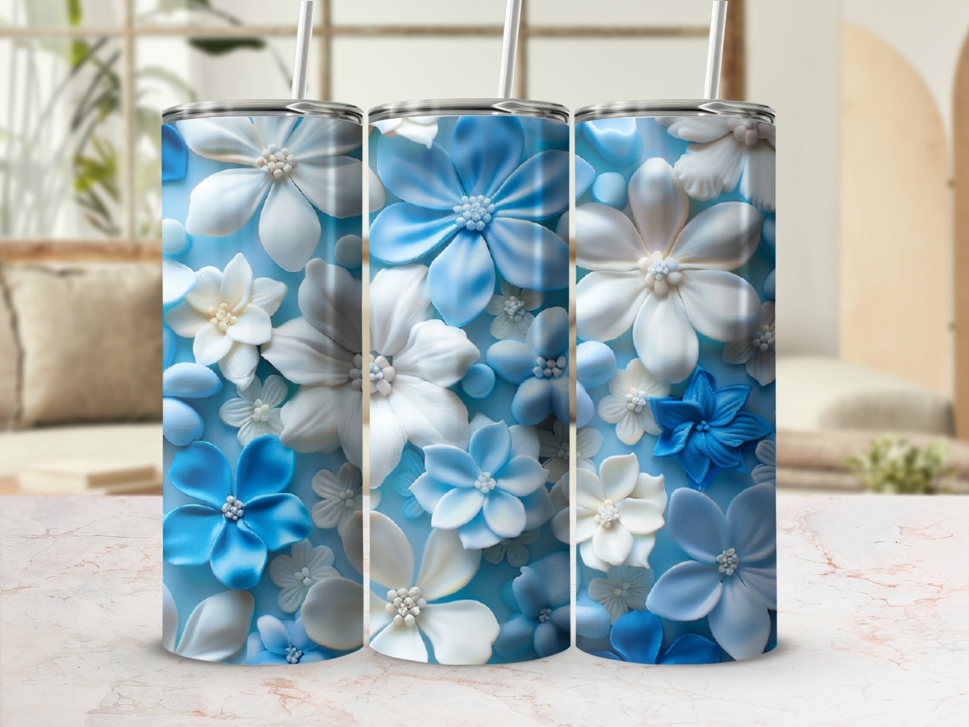 Three blue and white floral patterned tumblers with straws on a marbled surface.