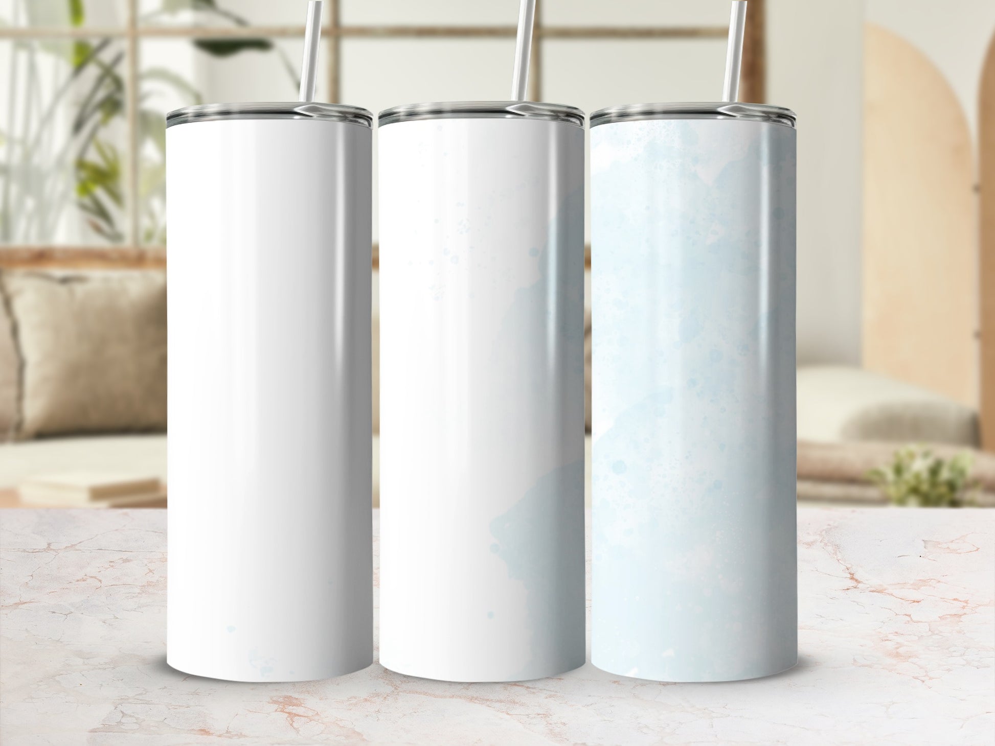 Three blank white and blue watercolor tumblers with straws on a marble surface.