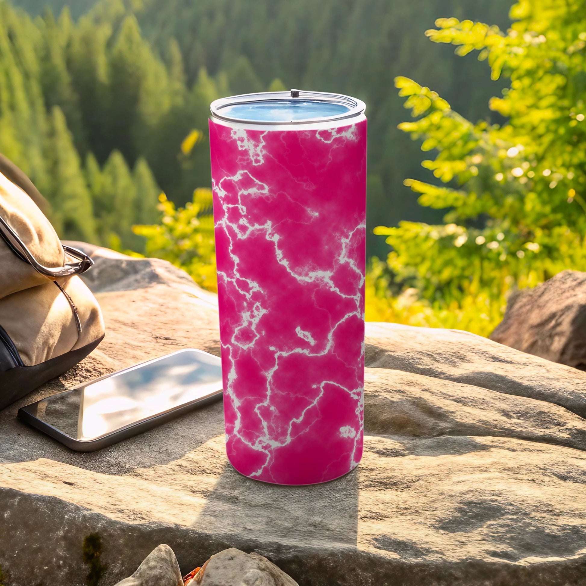 Pink marble pattern tumbler with a phone and backpack on rocks.