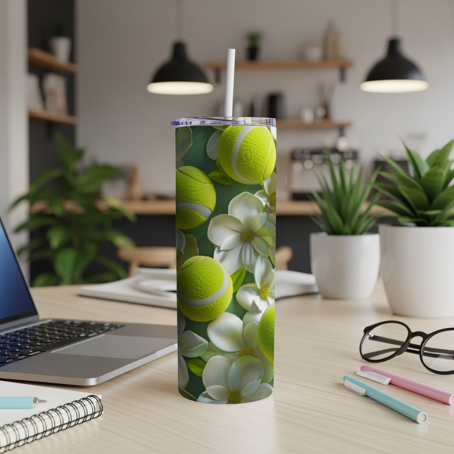Green tumbler with tennis balls and white flowers on a desk.