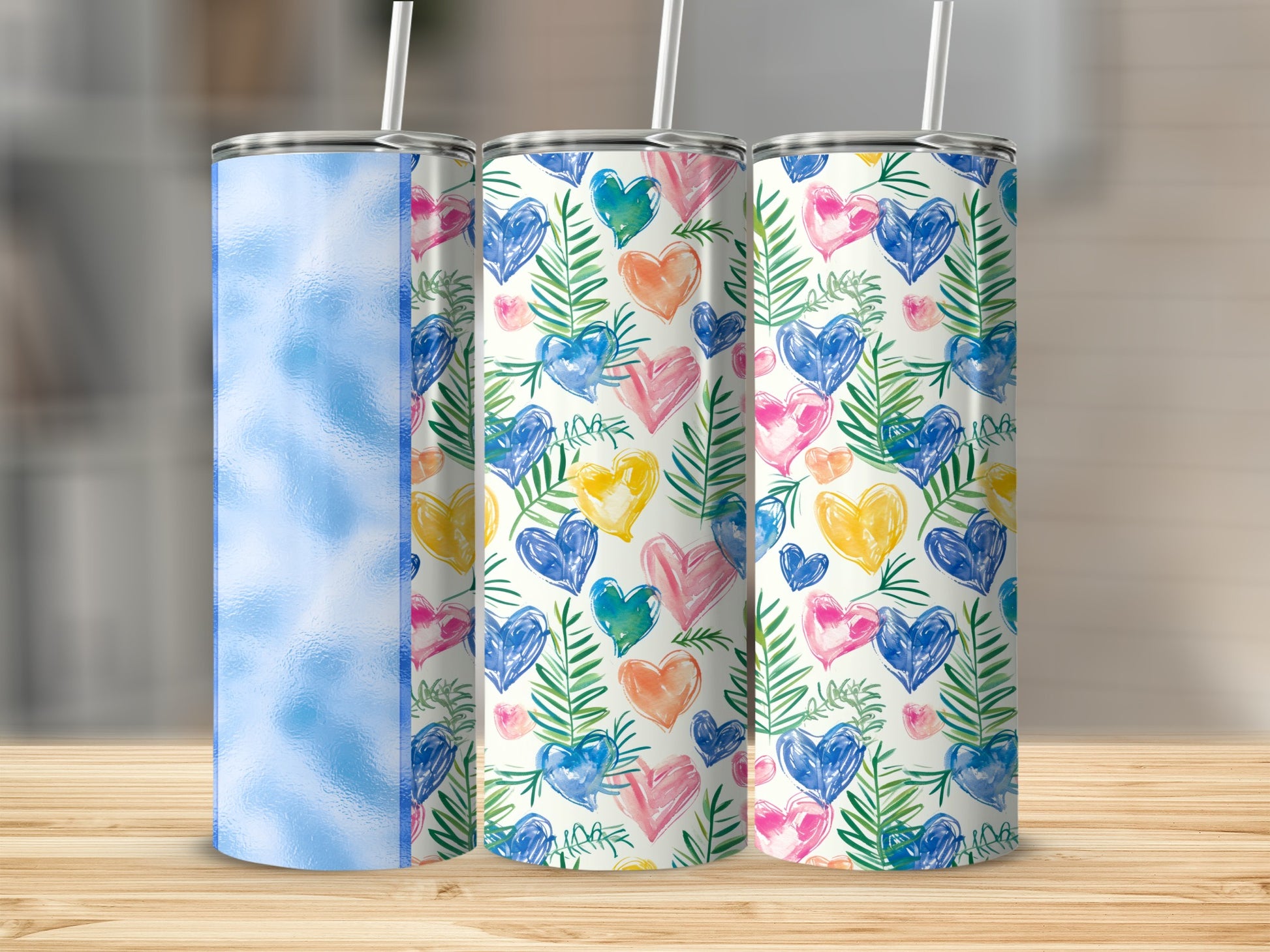 Three tumblers with colorful heart and leaf patterns on a wooden surface.