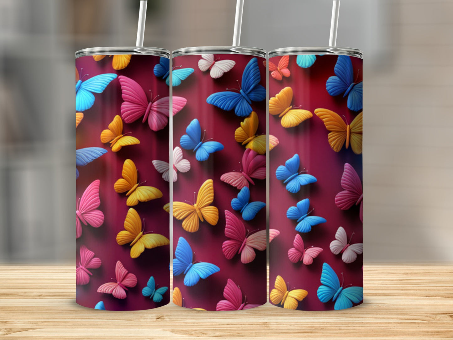 Three tumblers with colorful butterfly designs on a wooden surface.