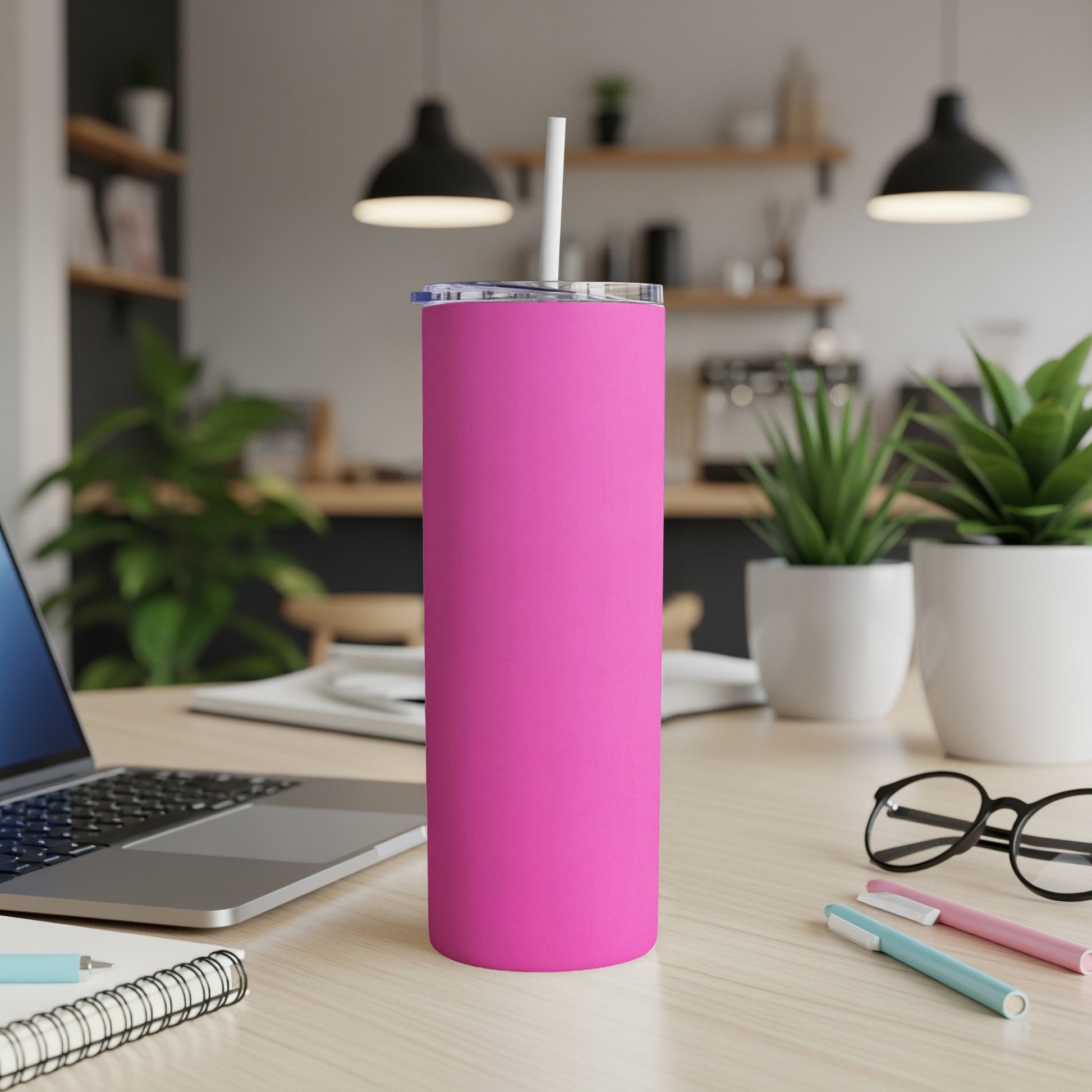 Pink tumbler with white straw on a desk with laptop and pens.