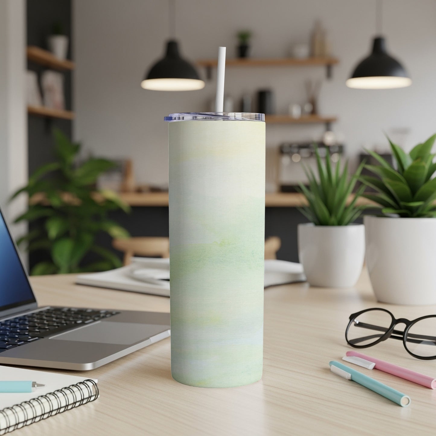 Tall, cylindrical tumbler with a pale green and yellow watercolor design, on a desk.