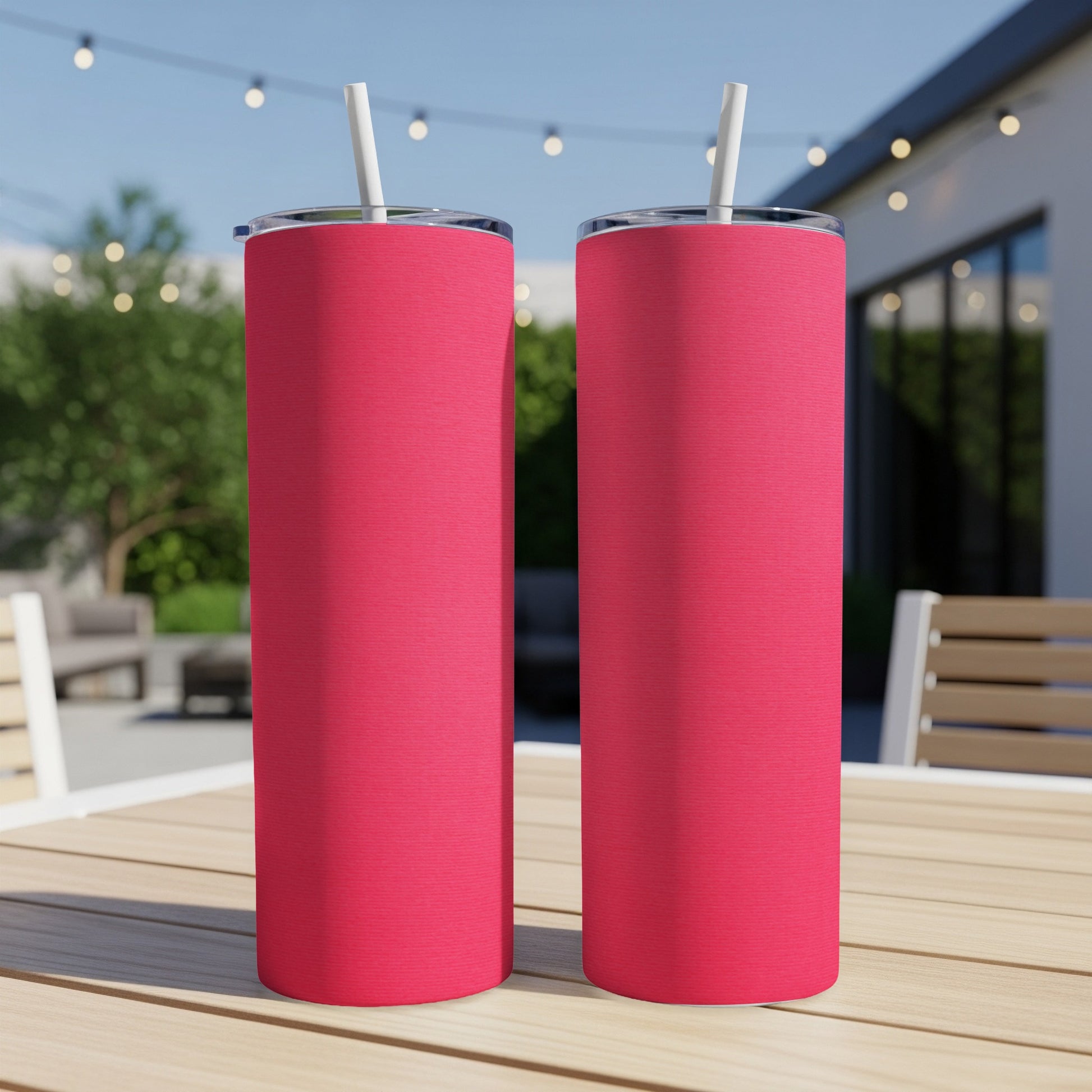 Two pink tumblers with straws sit on a wooden table.