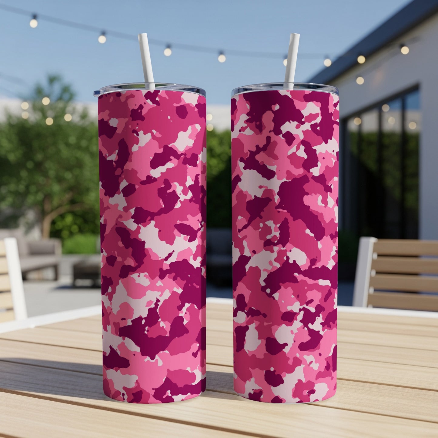 Two pink camouflage tumblers with white straws on a wooden table.