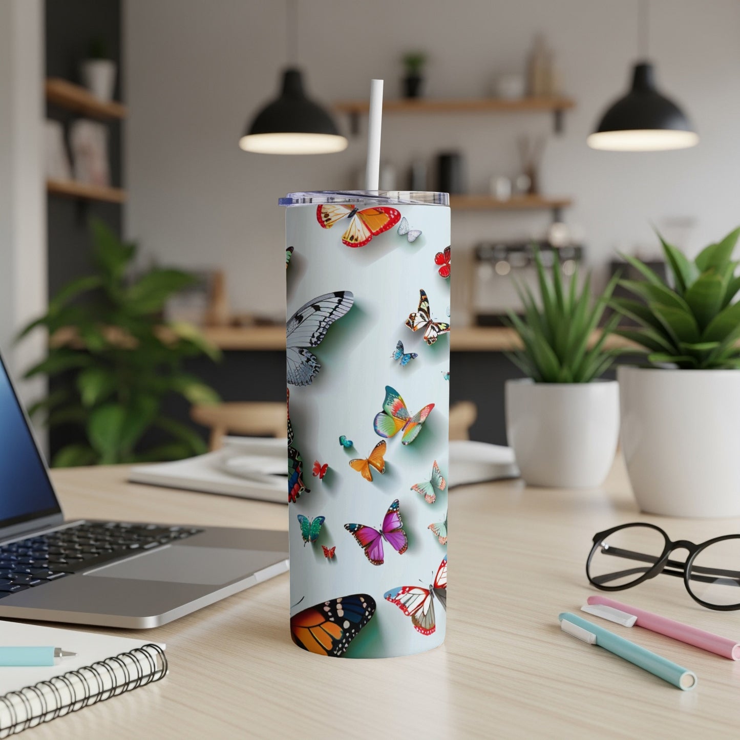 Tumbler with colorful butterflies and a straw on a desk.