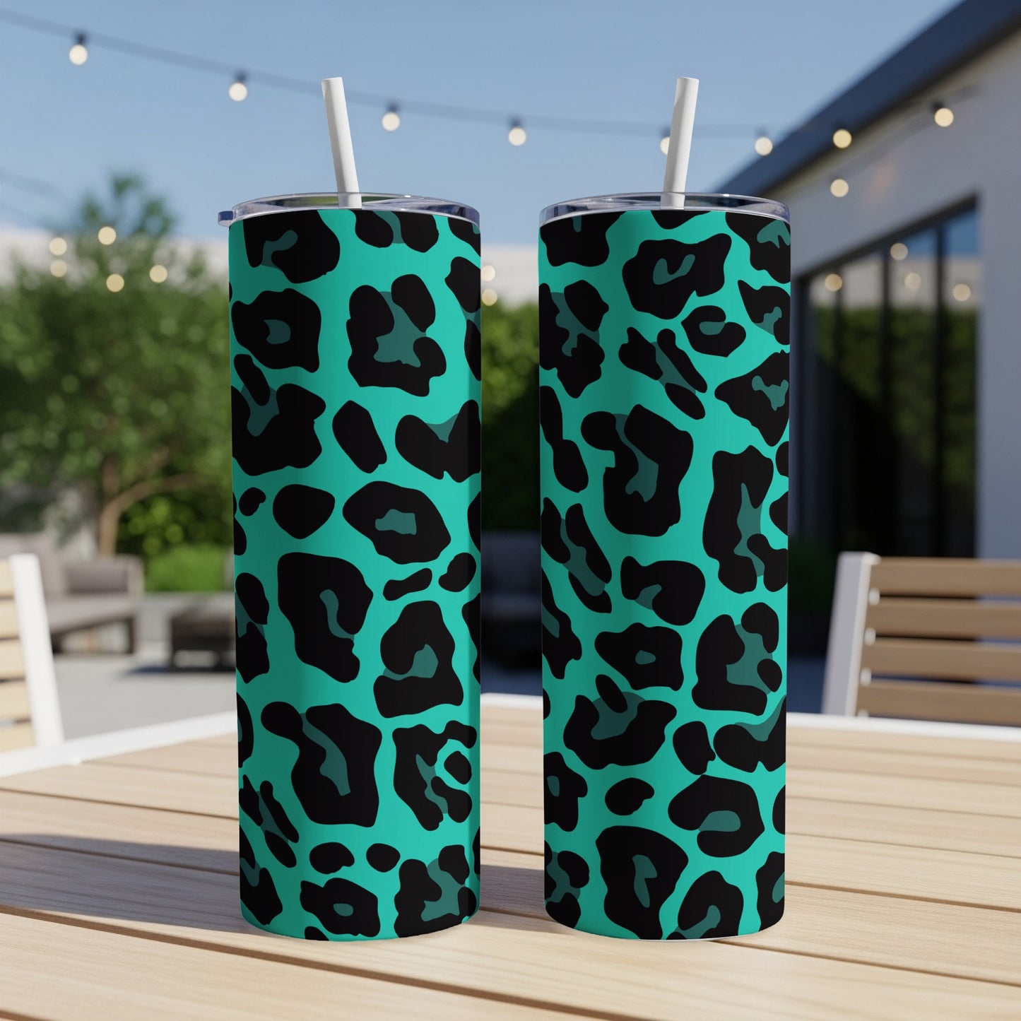 Two teal tumblers with black leopard print and white straws on a wooden table.