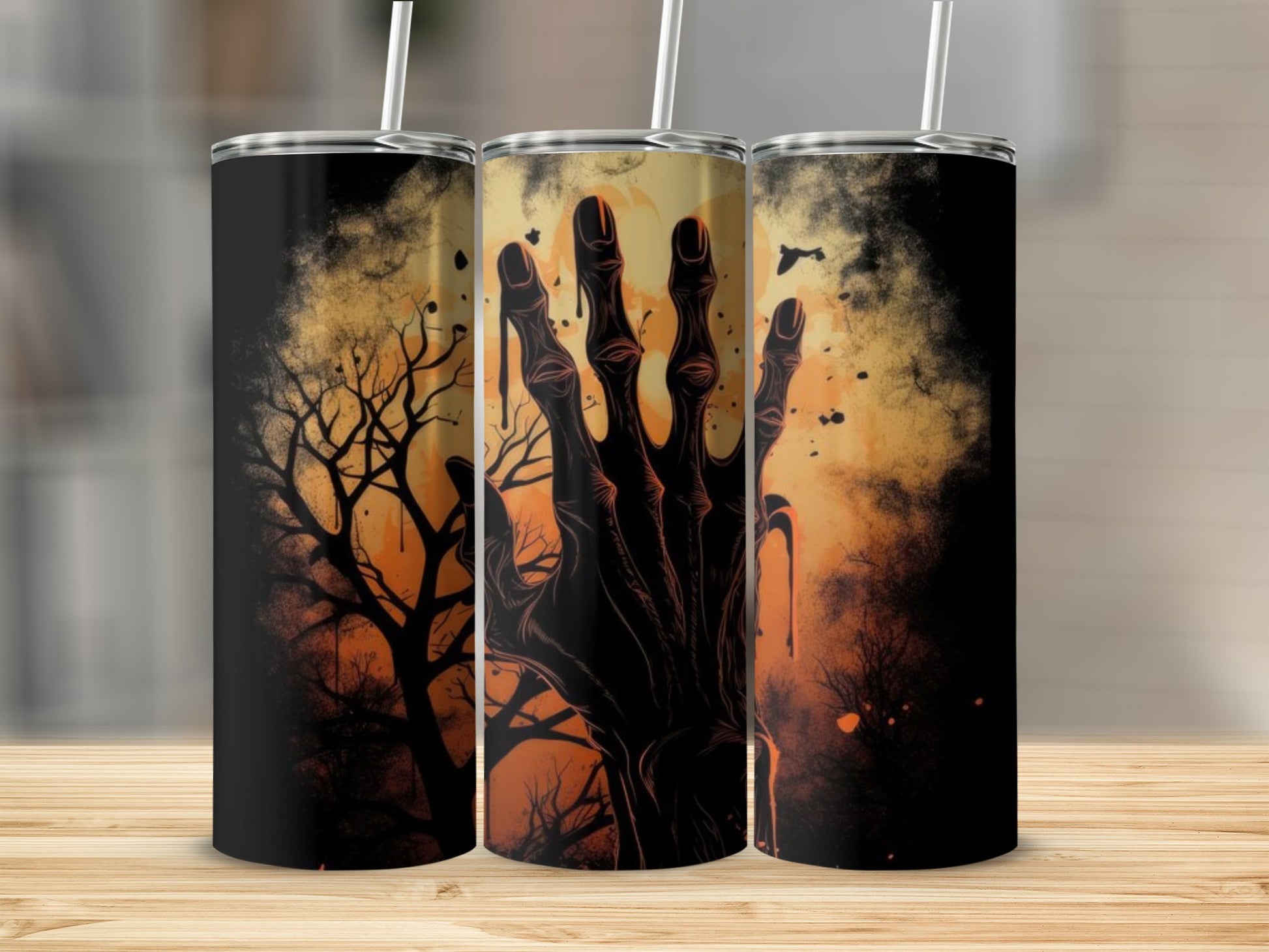 Three tumblers with a spooky hand and bare tree design on a warm, hazy background.