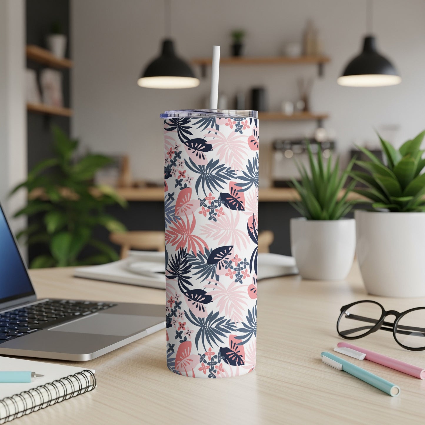Floral pattern tumbler with straw on desk with laptop and pens.