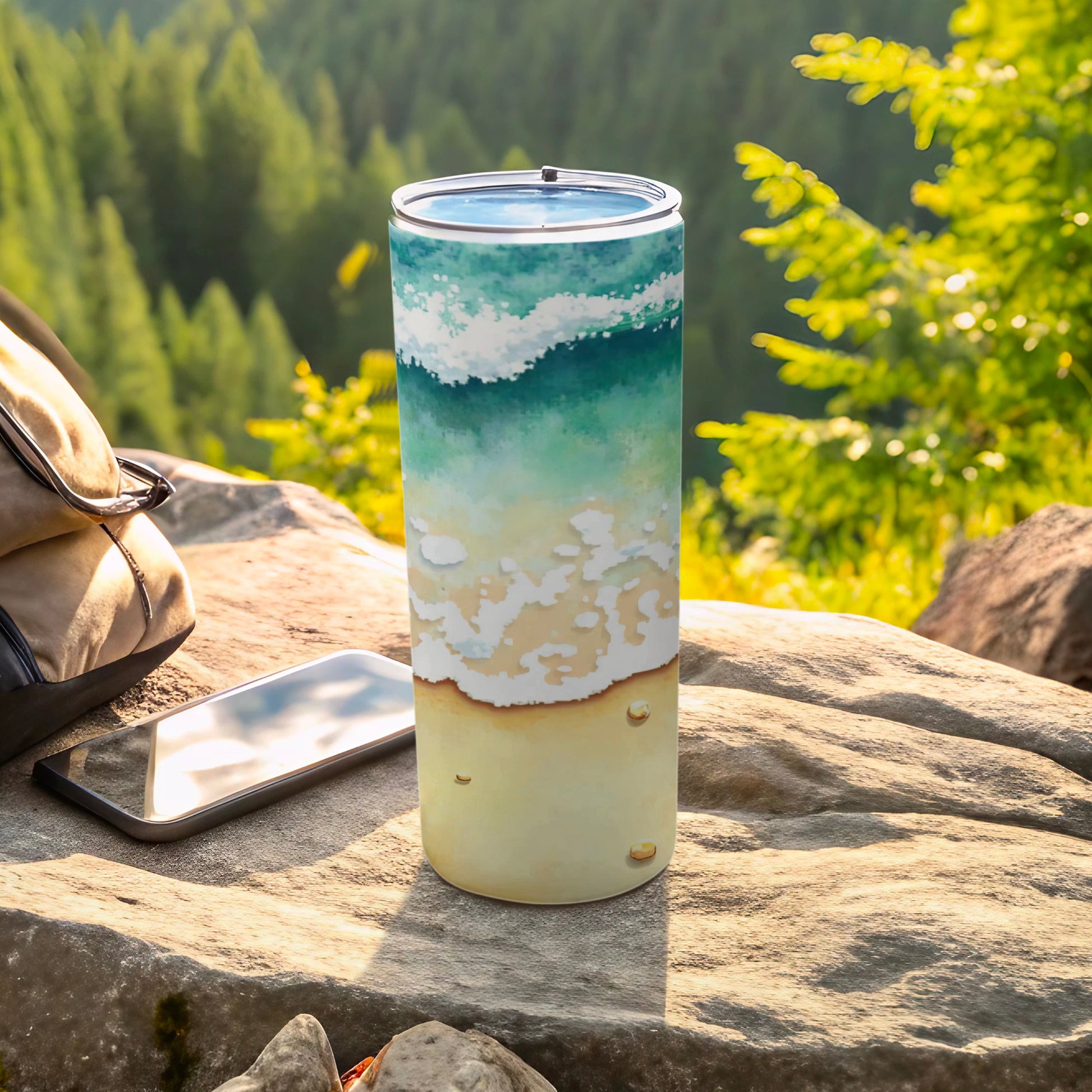 Tumbler with ocean wave and sand design, next to phone and bag.