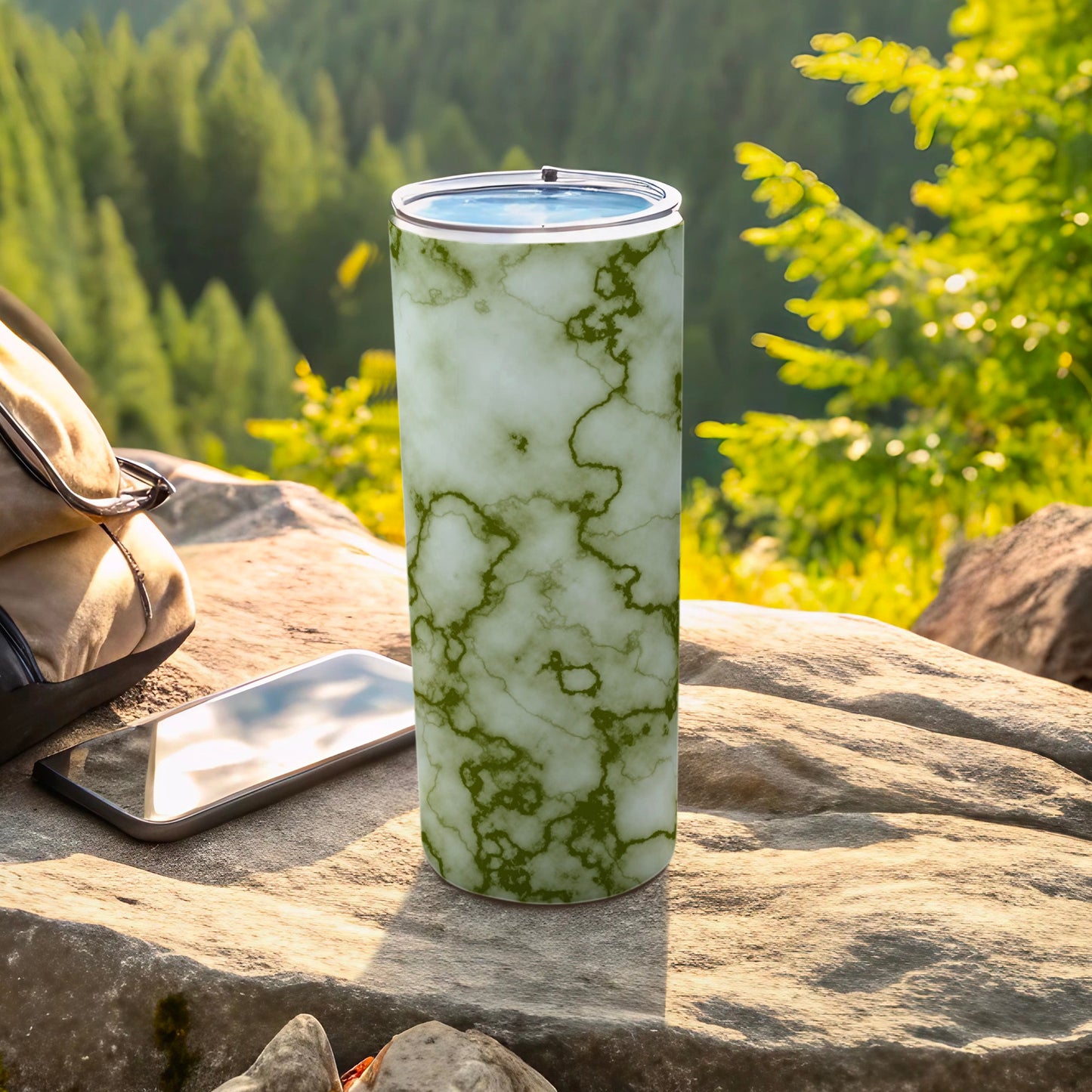 Marble-patterned tumbler with green veins rests on a rock, next to a phone.