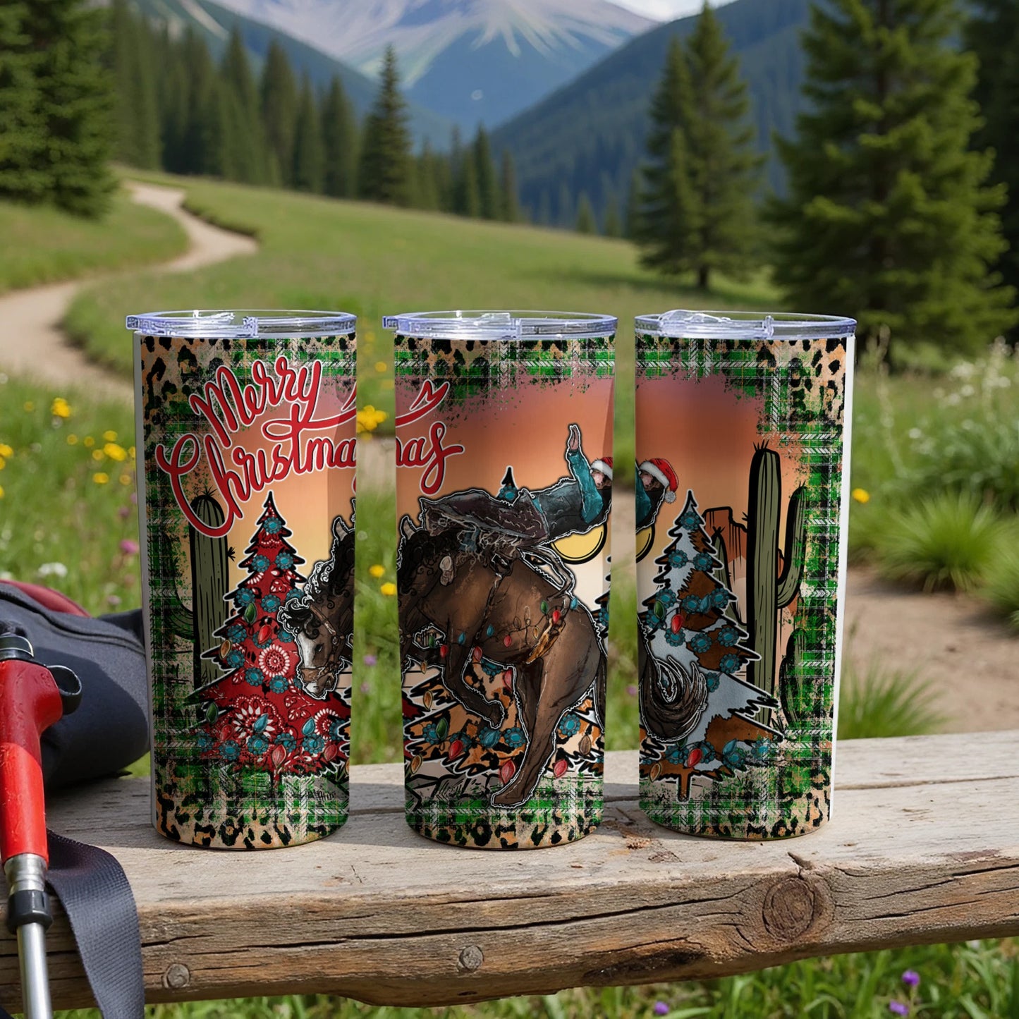 Three tumblers with Christmas and rodeo designs on a wooden table.