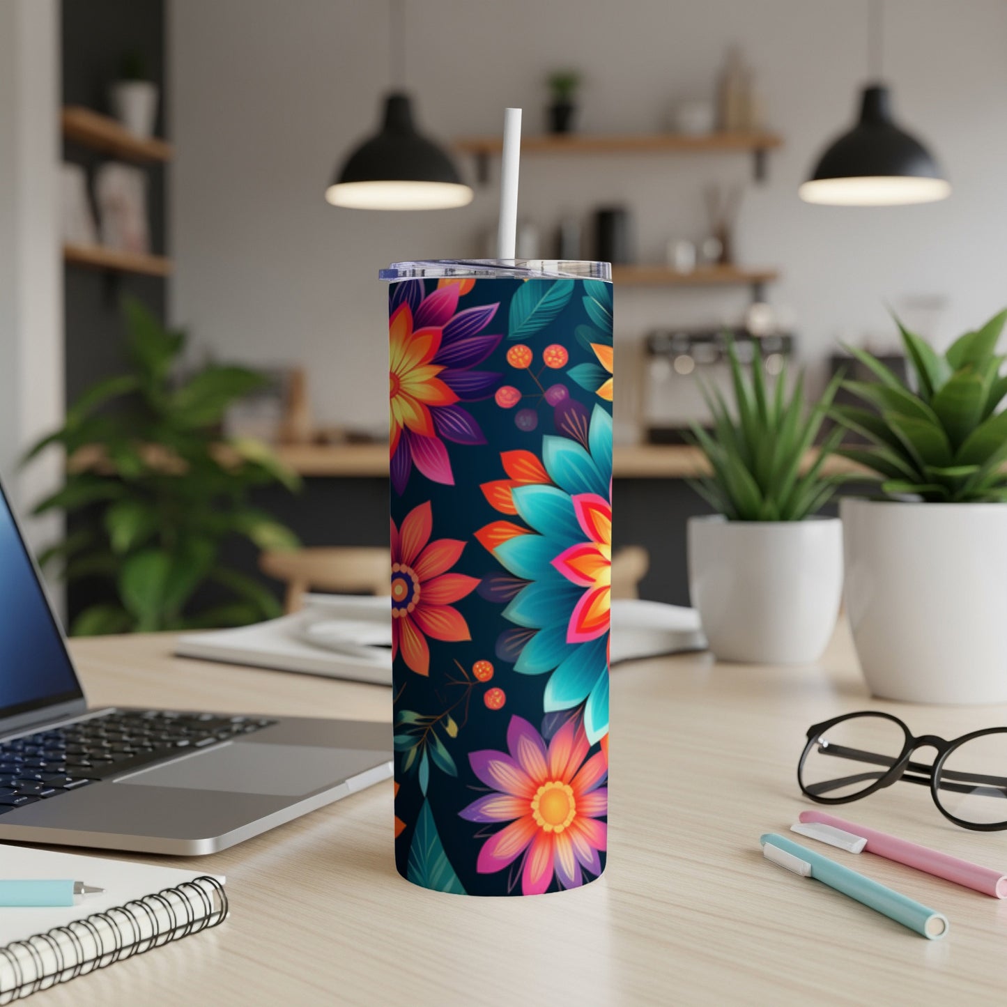 Floral patterned tumbler with straw on desk next to laptop and pens.