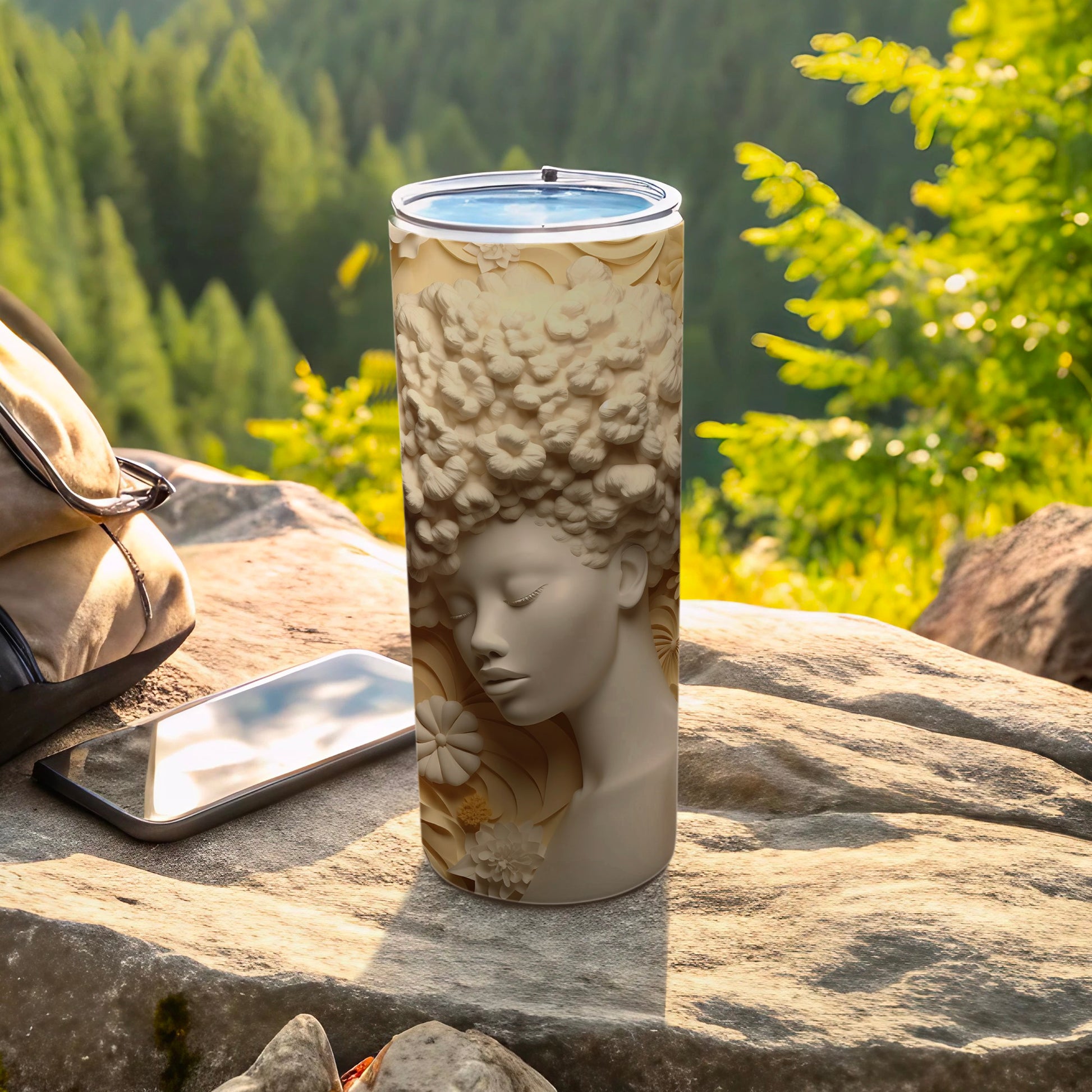Cream tumbler with raised floral relief of a woman's face, next to a phone and bag.