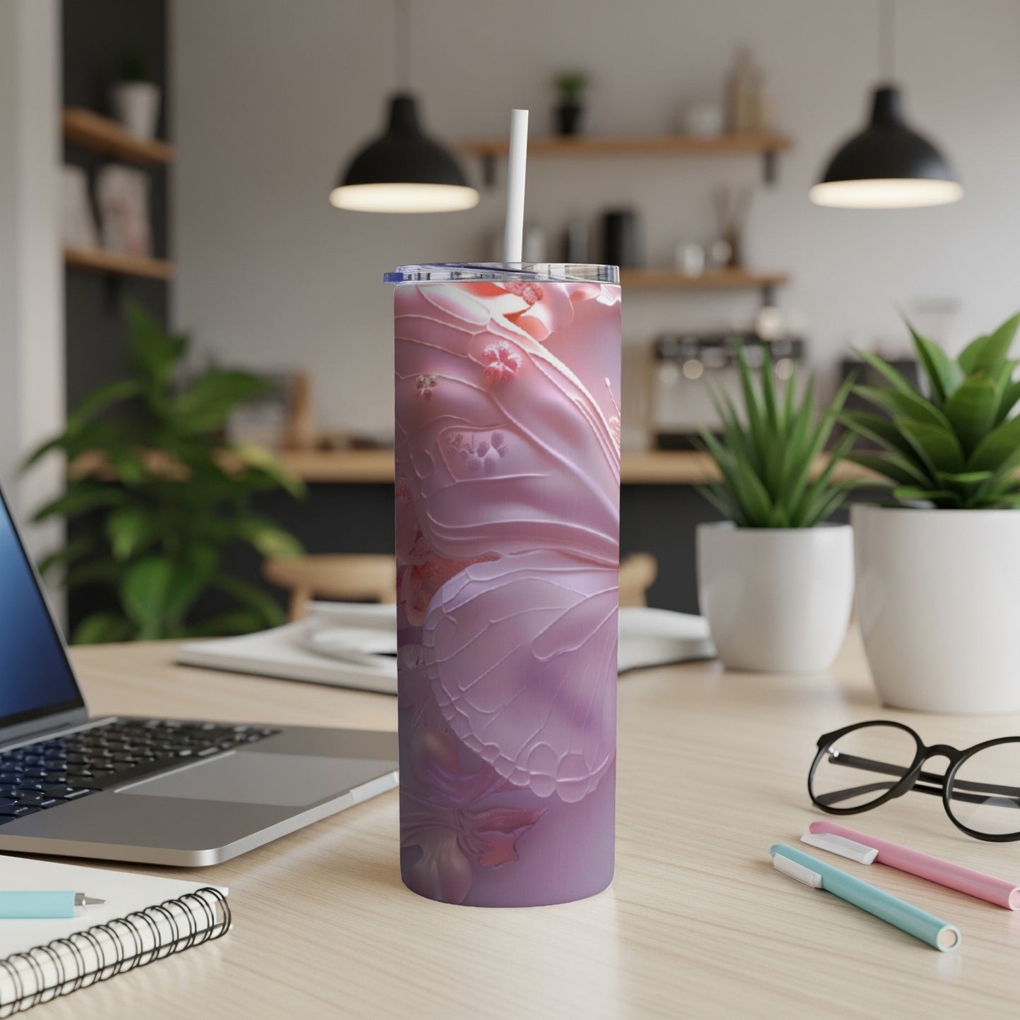 Pink floral design tumbler with straw on a desk with laptop and pens.