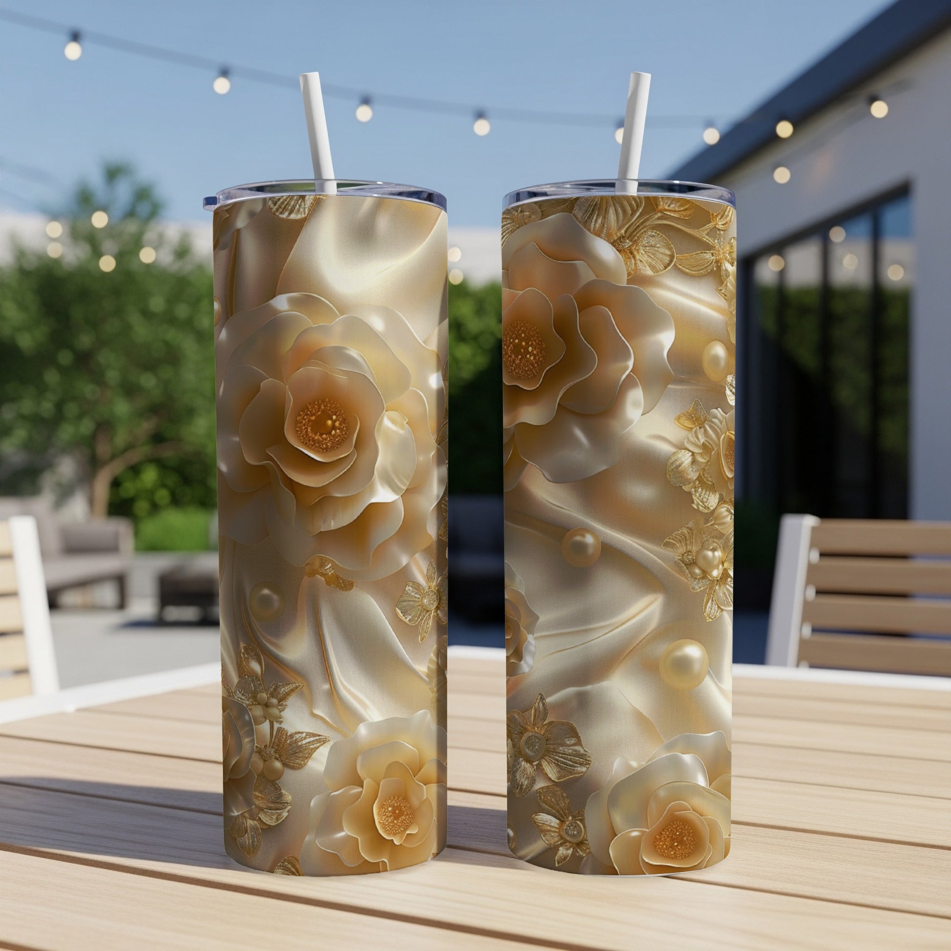 Two gold floral tumblers with straws on a wooden table outdoors.