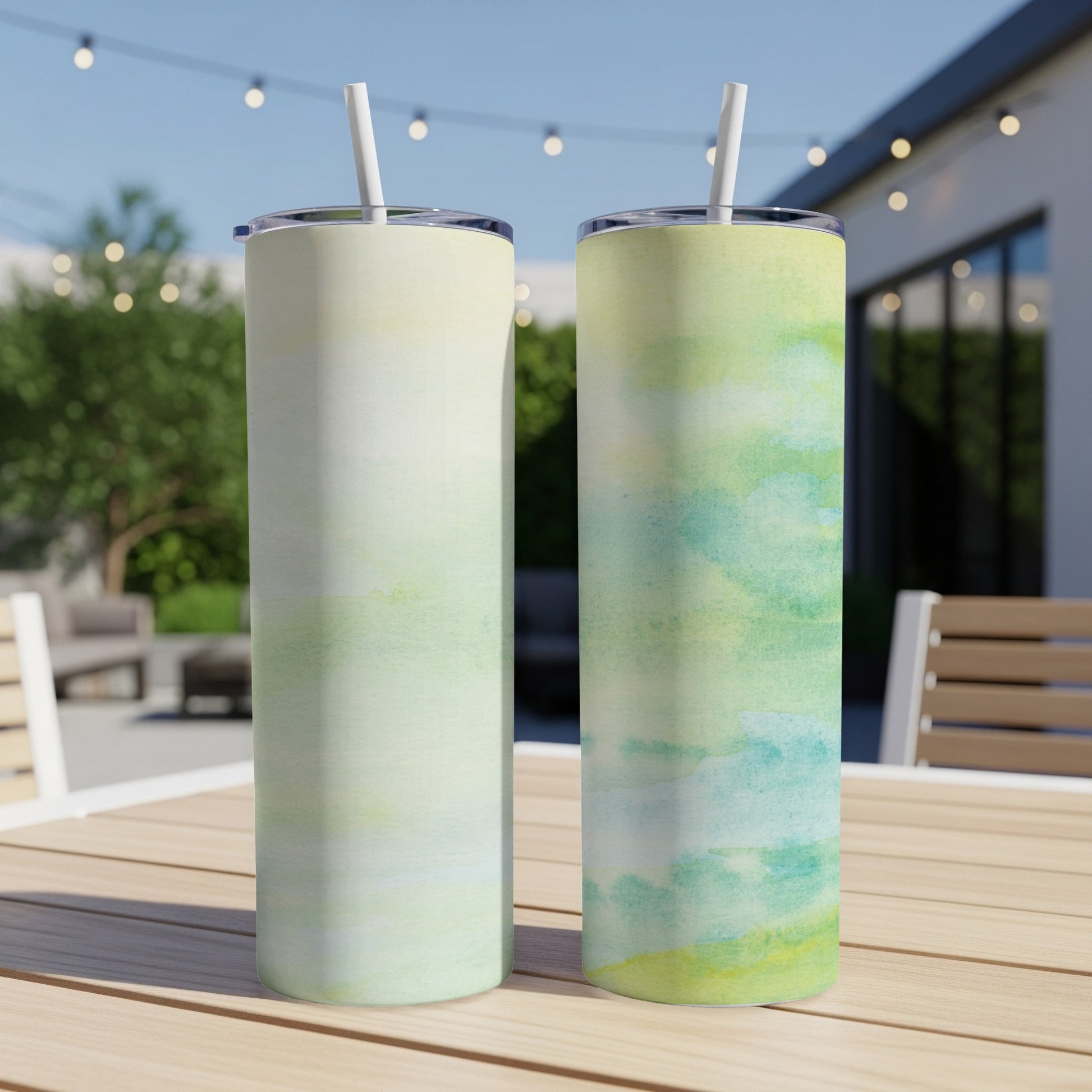 Two tall, slender tumblers with watercolor designs sit on a wooden table.