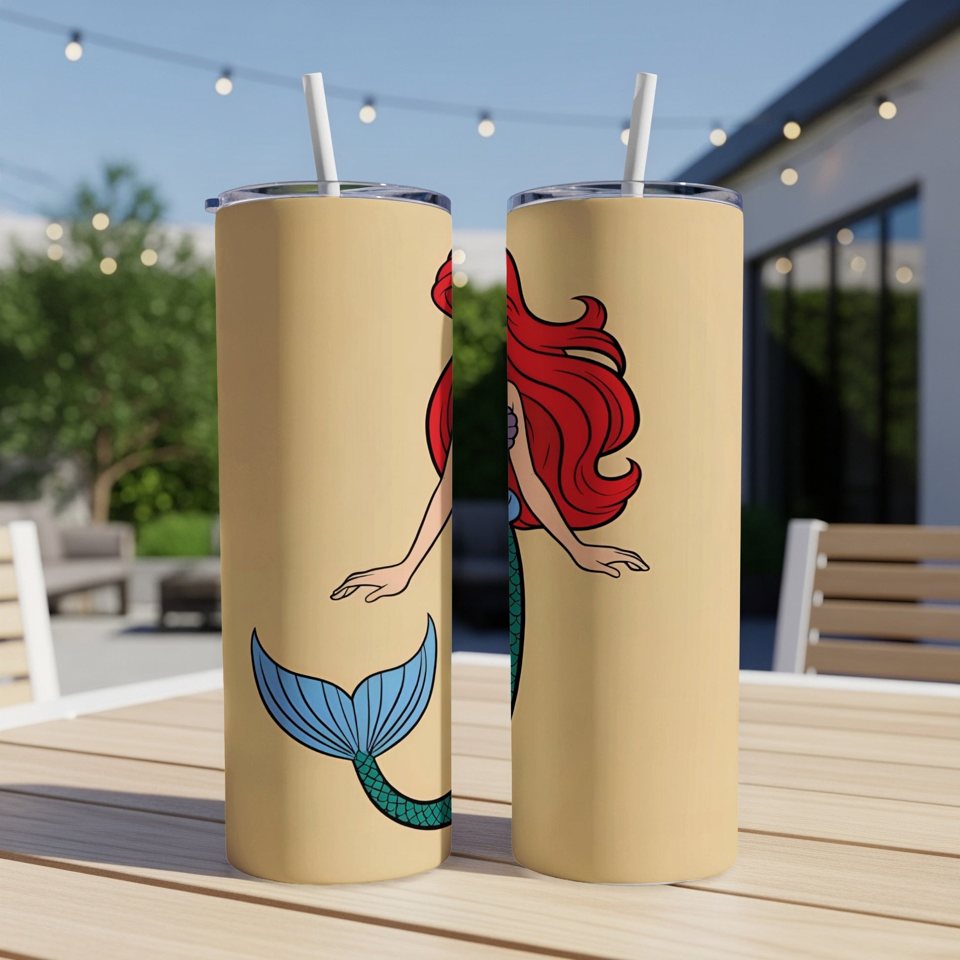 Two tan tumblers with Ariel the mermaid design on an outdoor table.