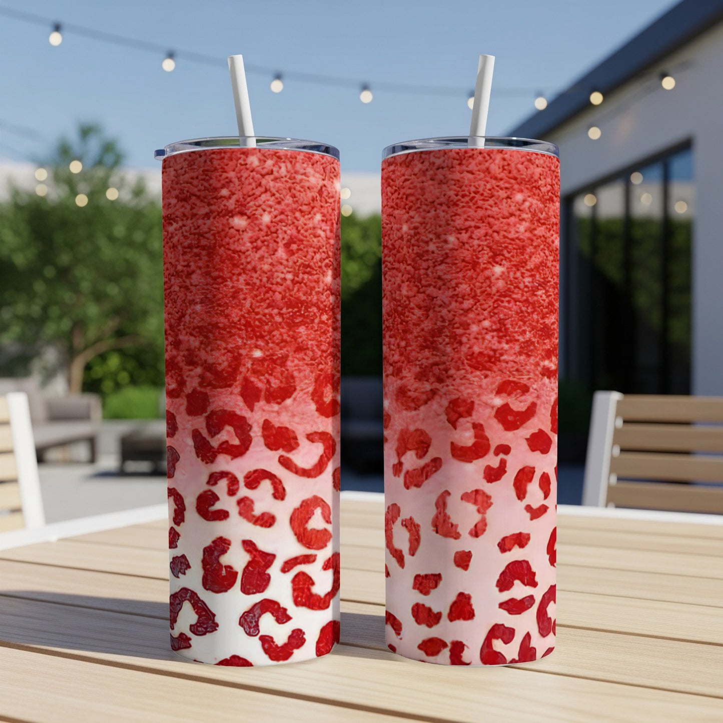 Two red glitter and leopard print tumblers with straws on a table.
