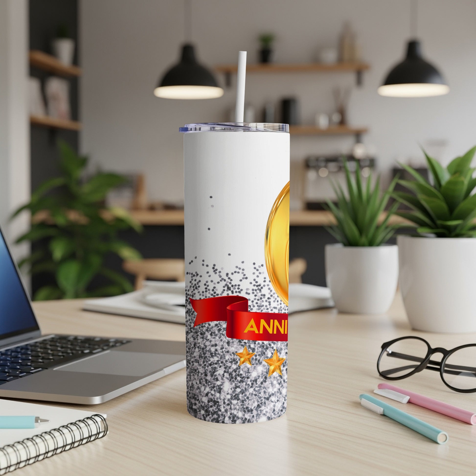 White tumbler with red ribbon and gold stars, "ANNIVERSARY" text on desk.