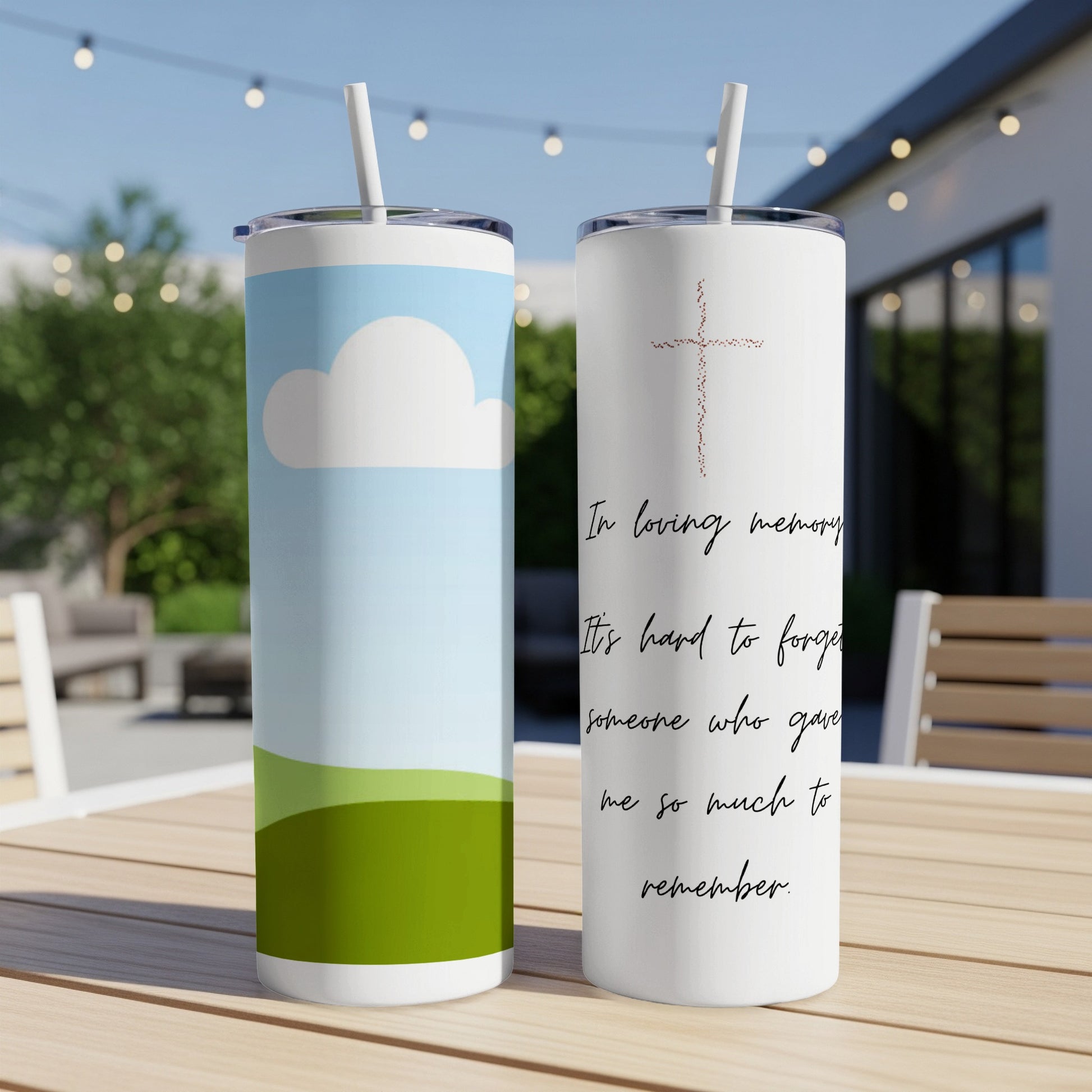 Two tumblers on a table, one with a cloud design, the other with a cross and memorial text.