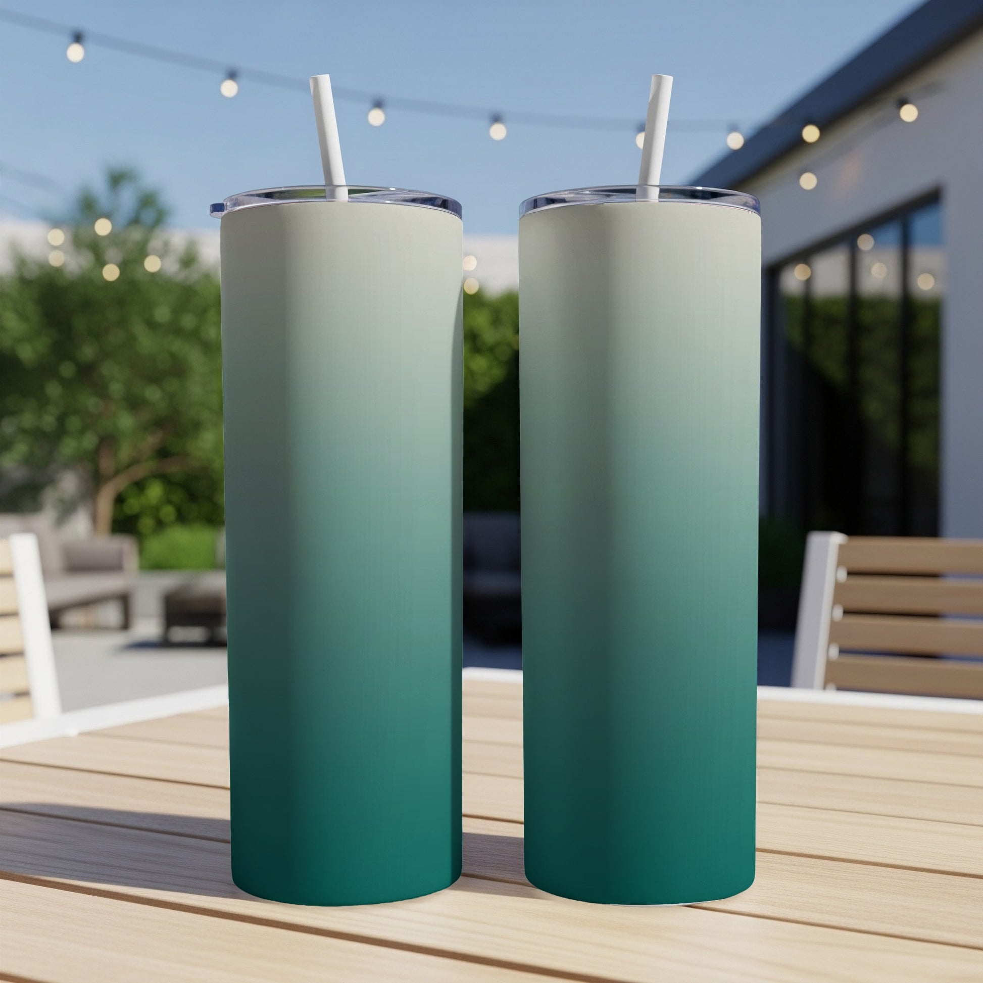Two gradient tumblers with straws on a wooden table outdoors.
