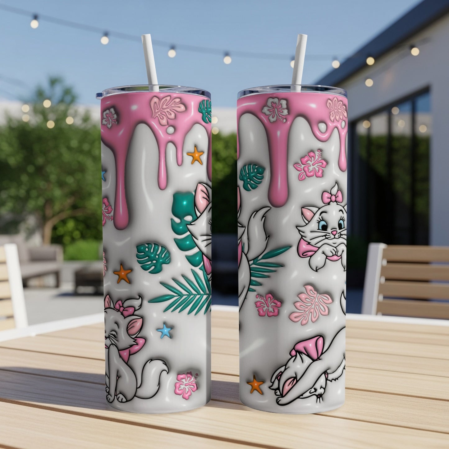 Two pink-dripping cat-themed tumblers with straws on a table.