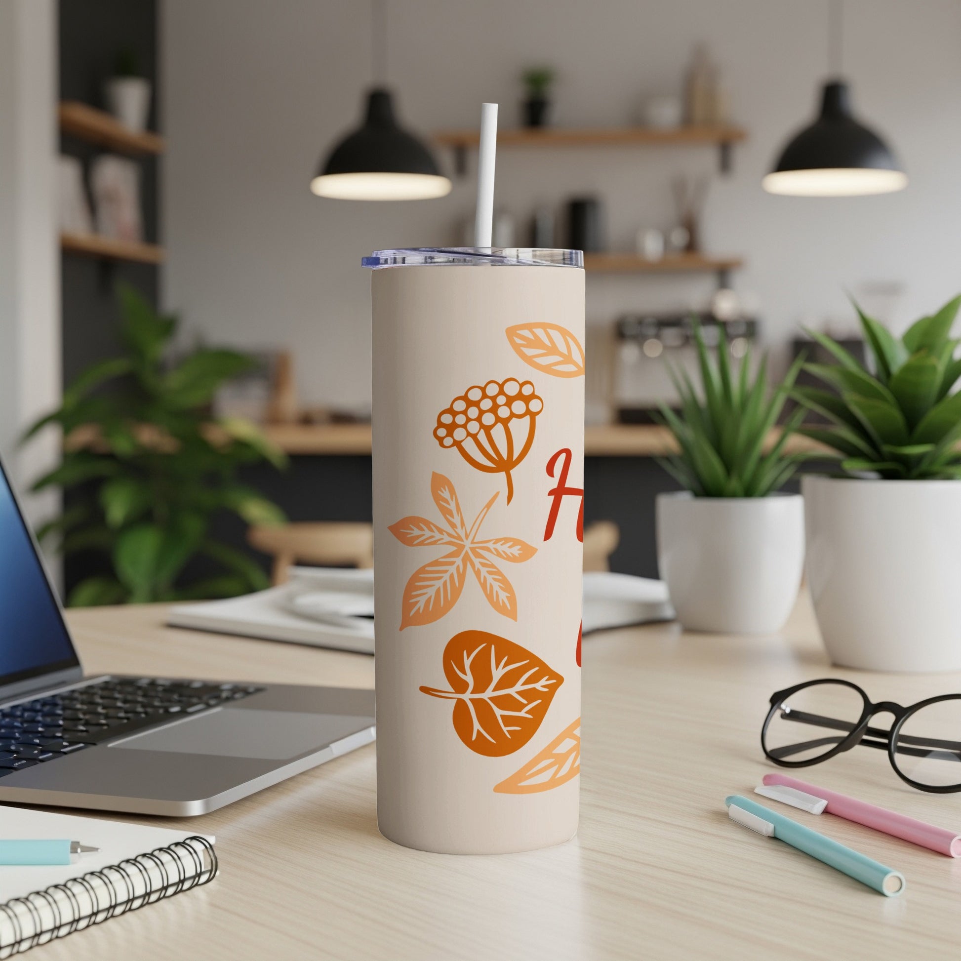 Beige tumbler with fall leaf designs and straw on a desk.
