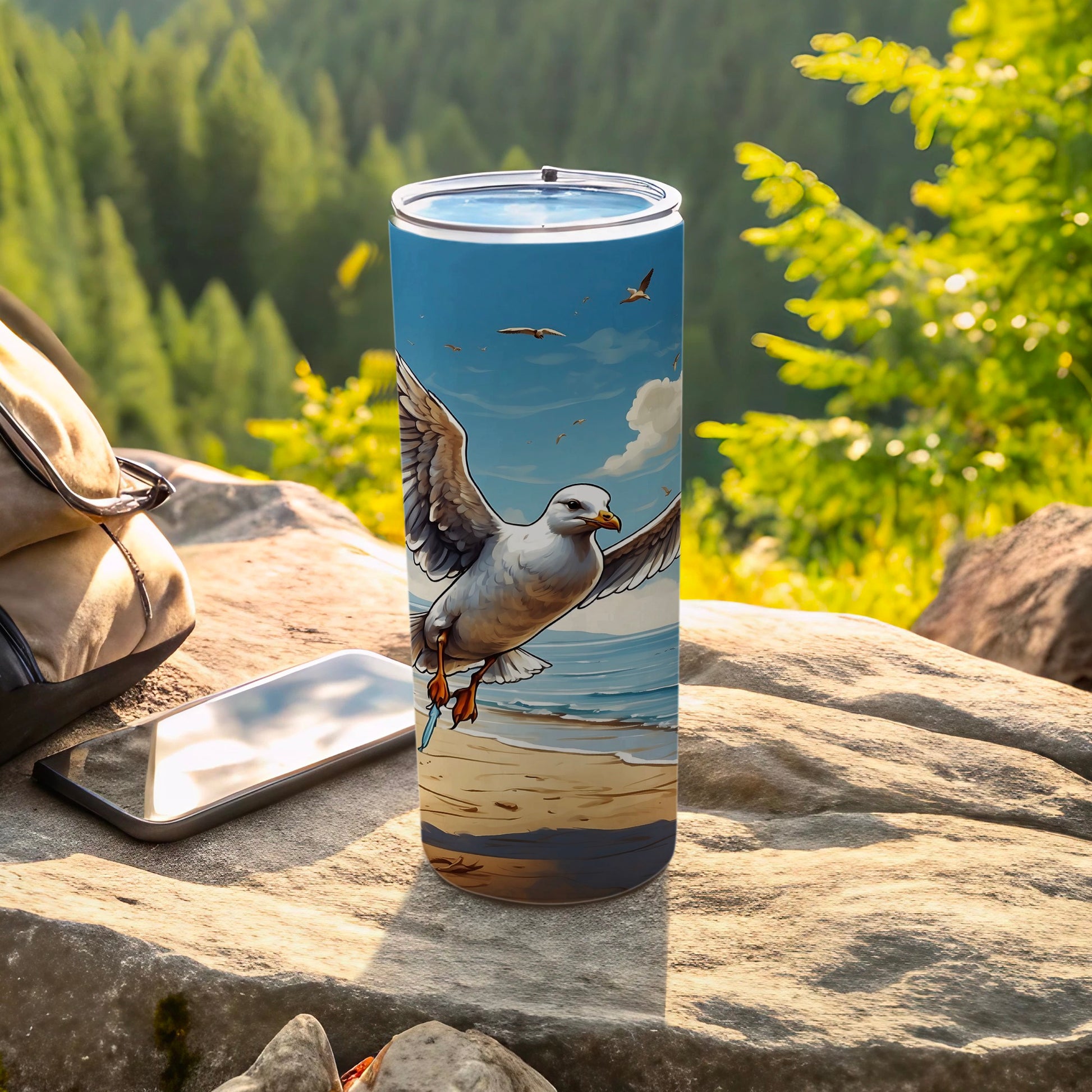 Seagull soaring over a beach on a skinny tumbler, next to a backpack and phone.
