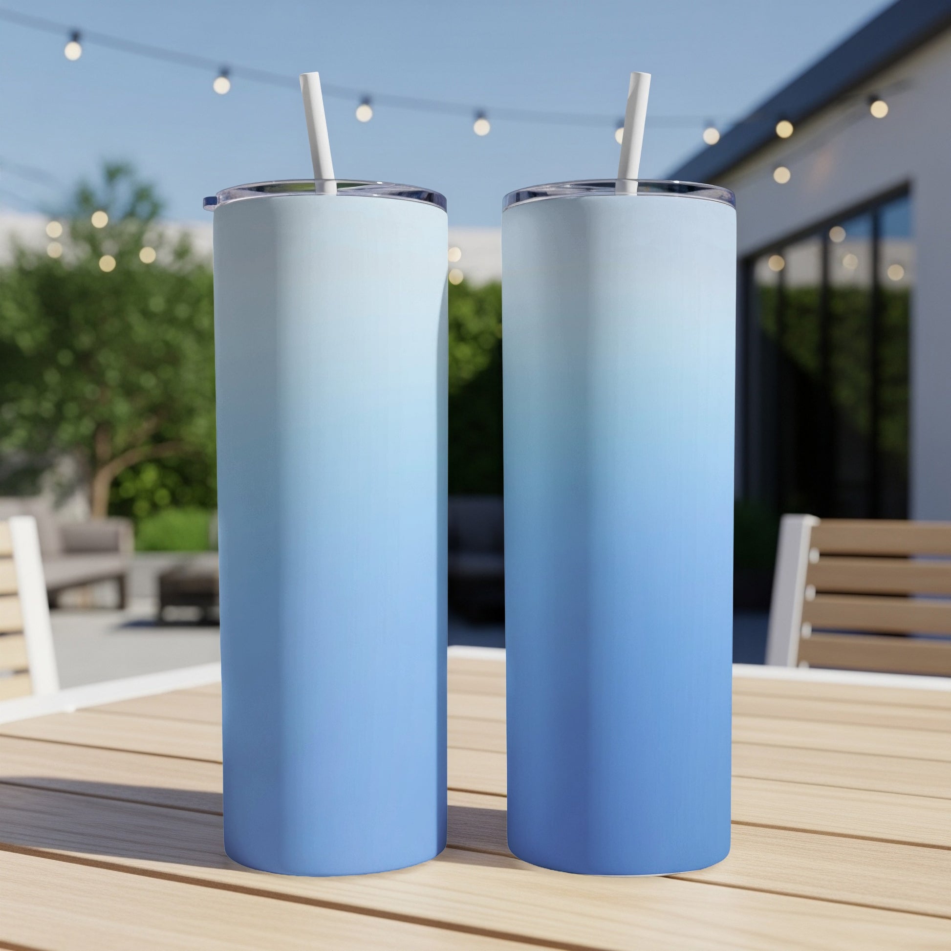 Two blue ombre tumblers with straws on a wooden table outdoors.