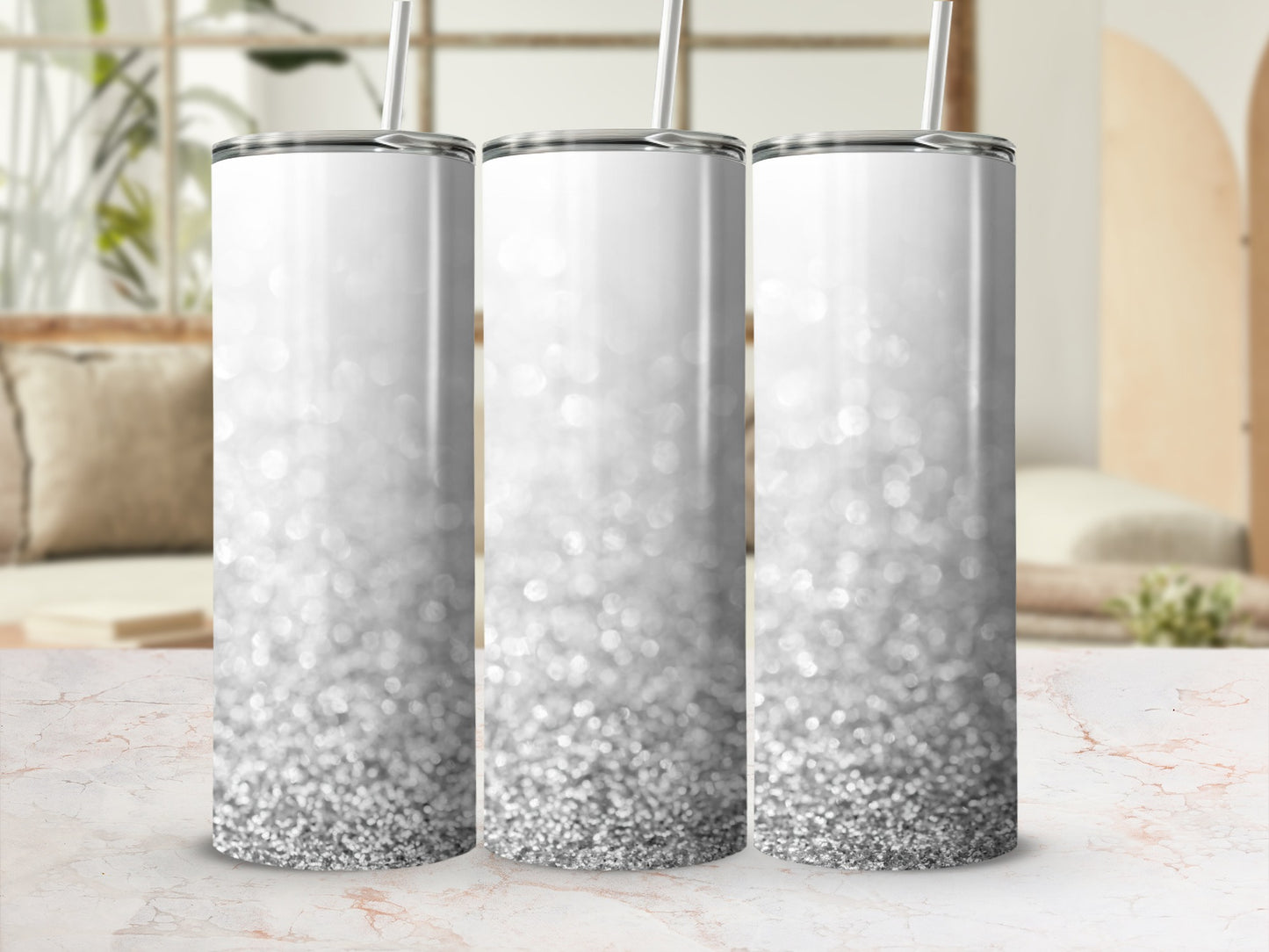 Three silver glitter tumblers with straws on a marble countertop.