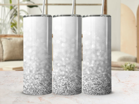 Three silver glitter tumblers with straws on a marble countertop.