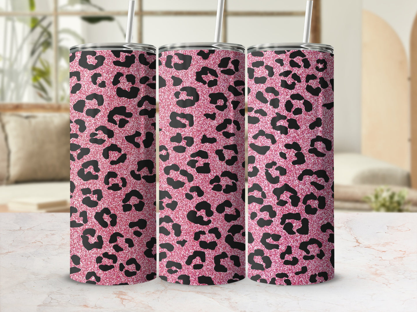 Three pink leopard print tumblers with straws on a marble surface.