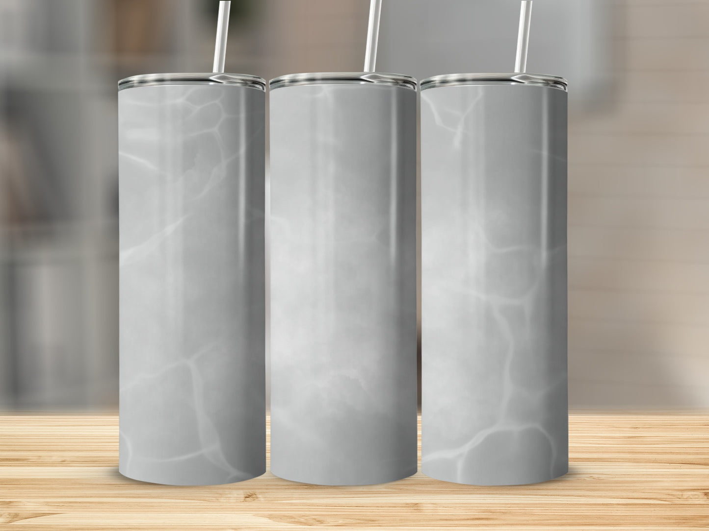 Three marble-patterned tumblers with straws on a wooden surface.
