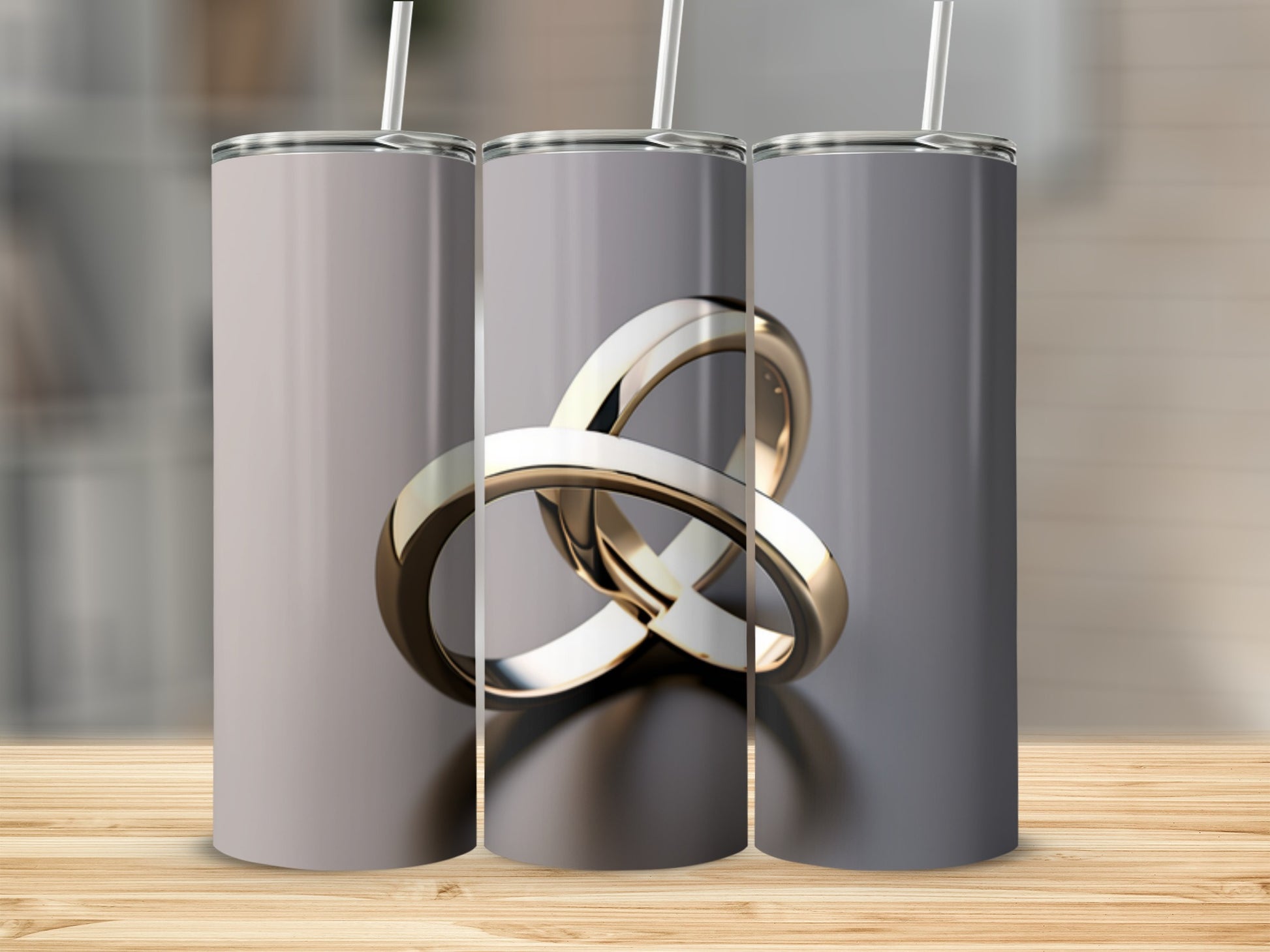 Three silver tumblers with intertwined gold rings design on a wooden surface.