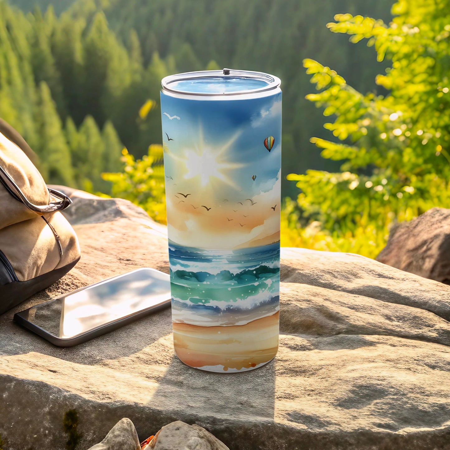 Tumbler with a beach sunset scene, hot air balloon, and birds, placed on rocks.