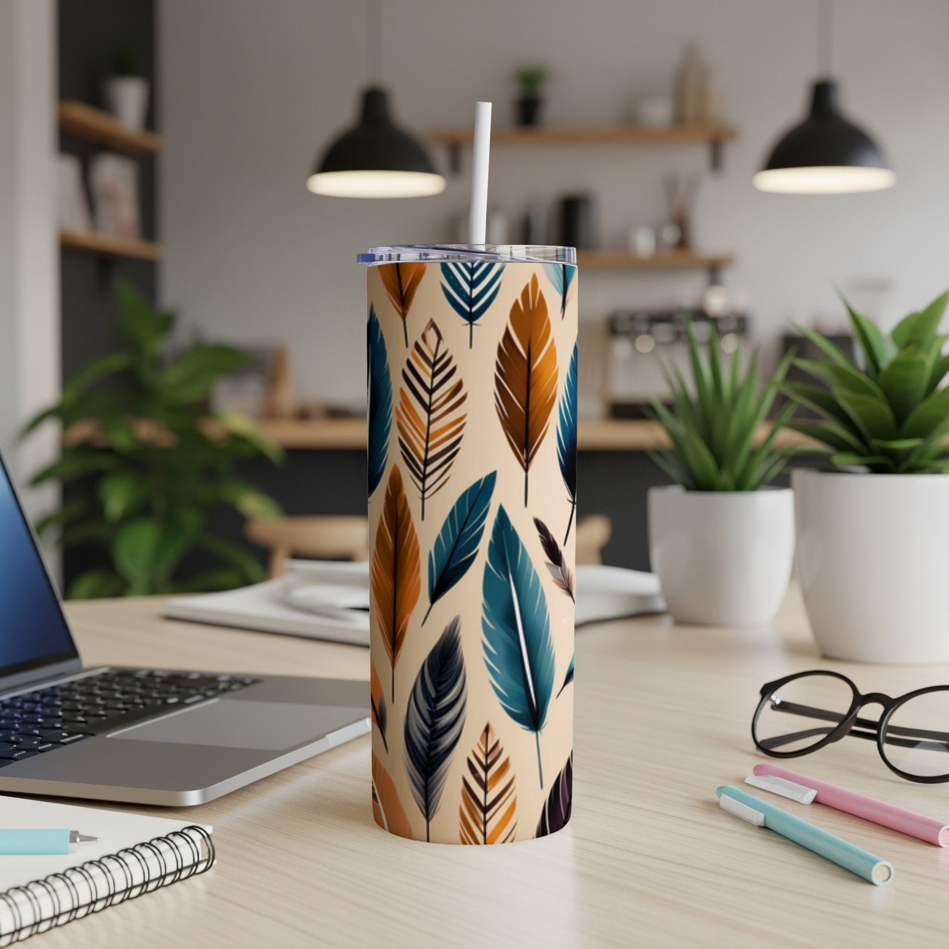 Tall tumbler with colorful feather pattern, straw, and pens on desk.