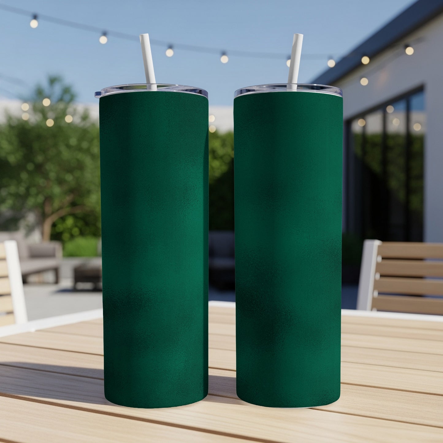 Two tall, dark green tumblers with white straws sit on a wooden table outdoors.