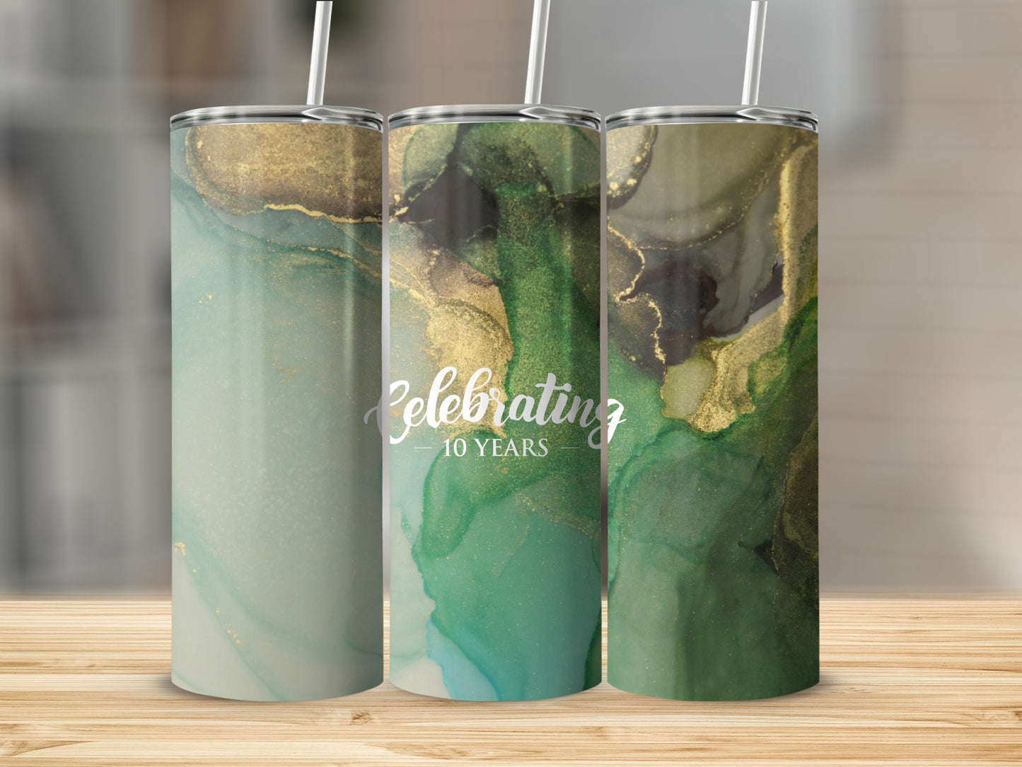 Three tumblers with abstract green and gold watercolor designs and "Celebrating 10 Years" text.