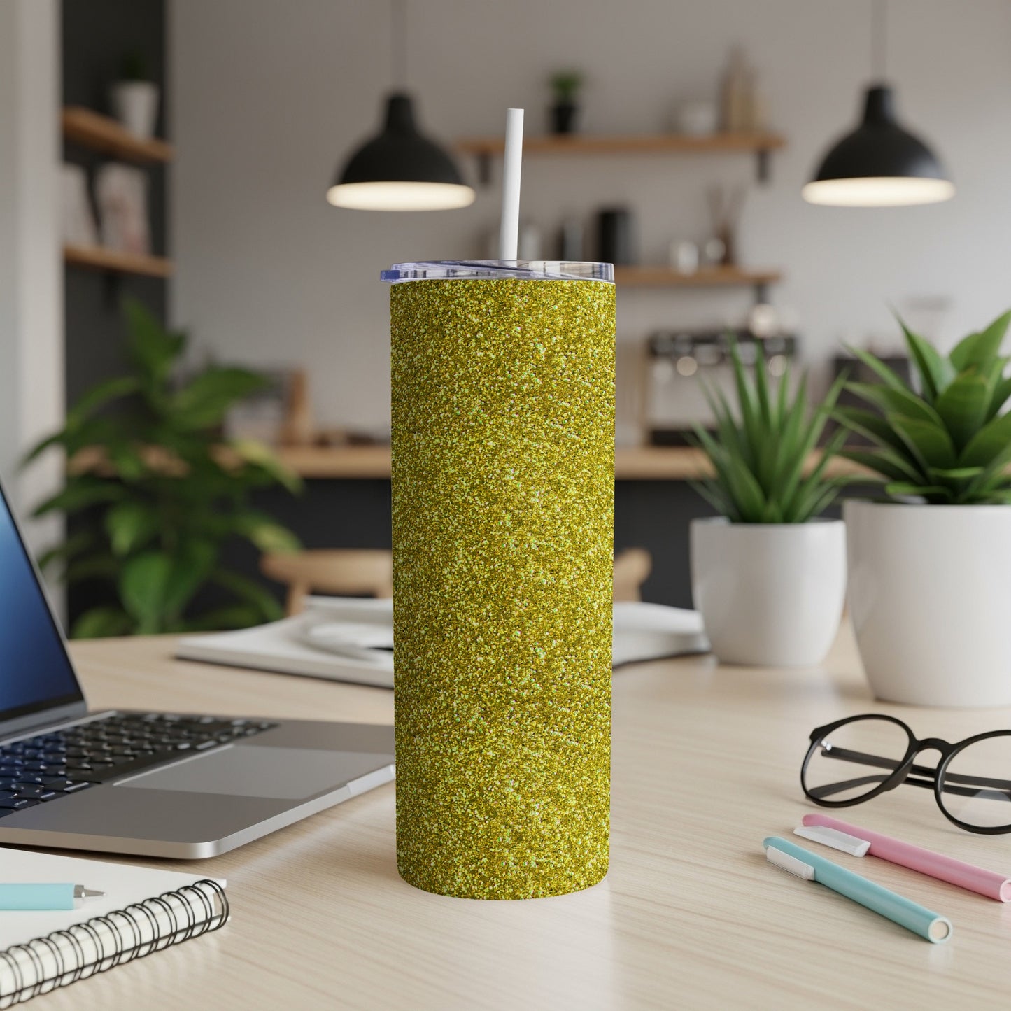 Glittery gold tumbler with straw on a desk with a laptop and plants.