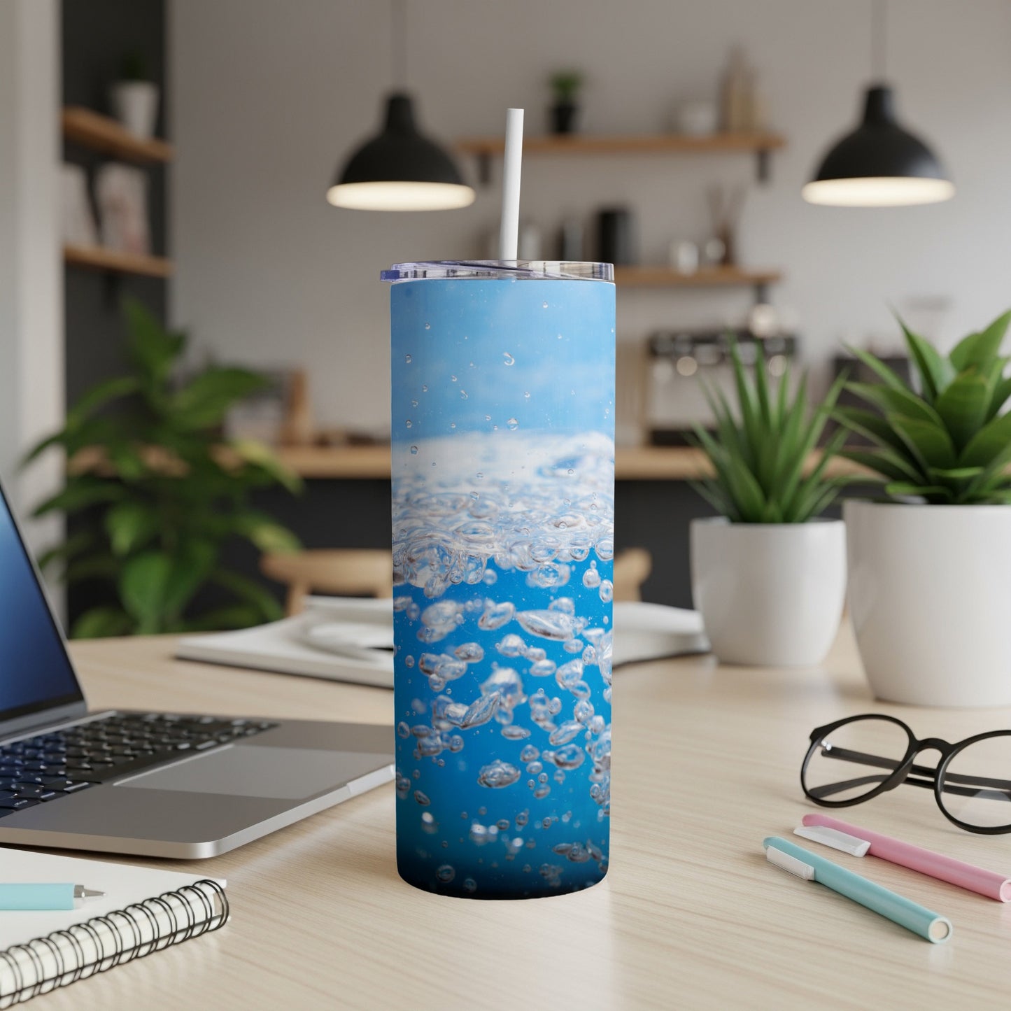 Blue tumbler with bubbles and straw, placed on a desk.